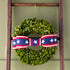 Green wreath with a red, white, and blue ribbon tied in a bow on a wooden ladder against a green wall.