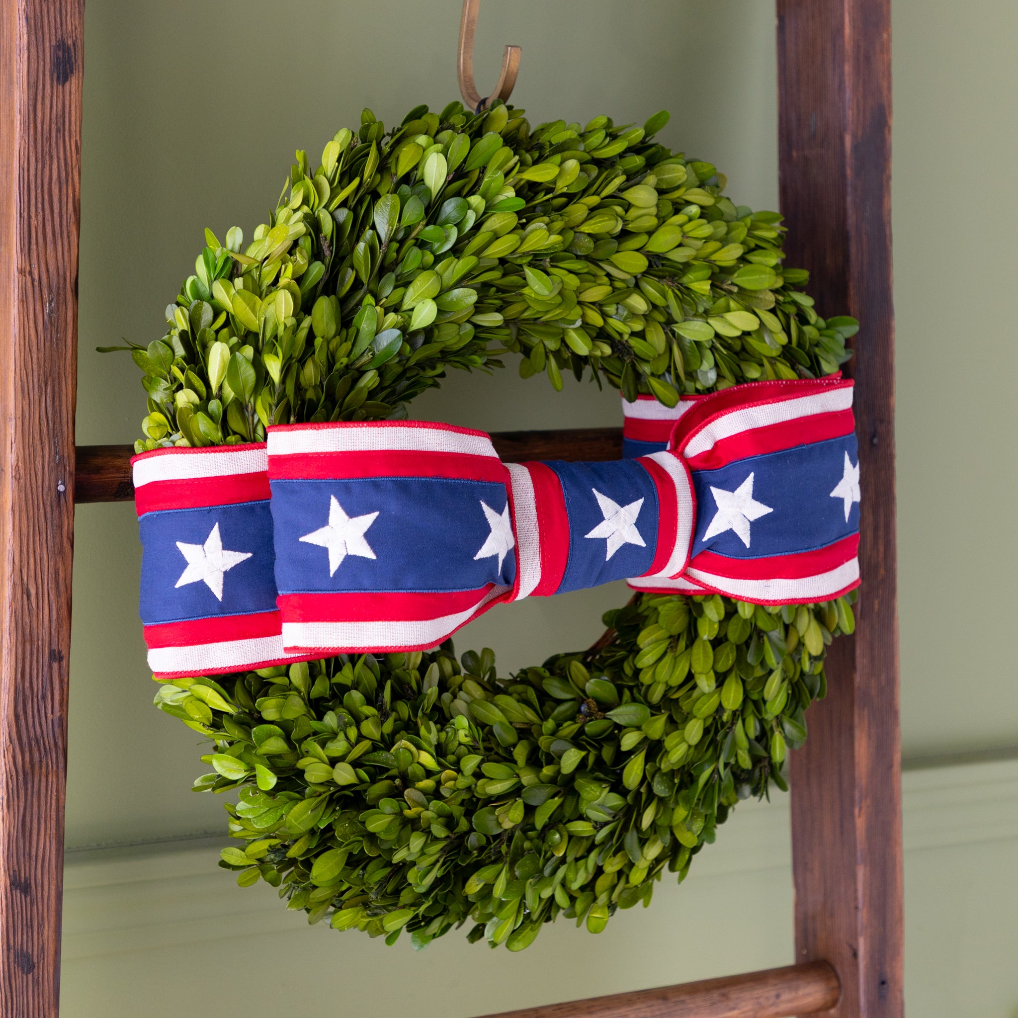 Green wreath with a red, white, and blue ribbon on a wooden ladder against a green wall.