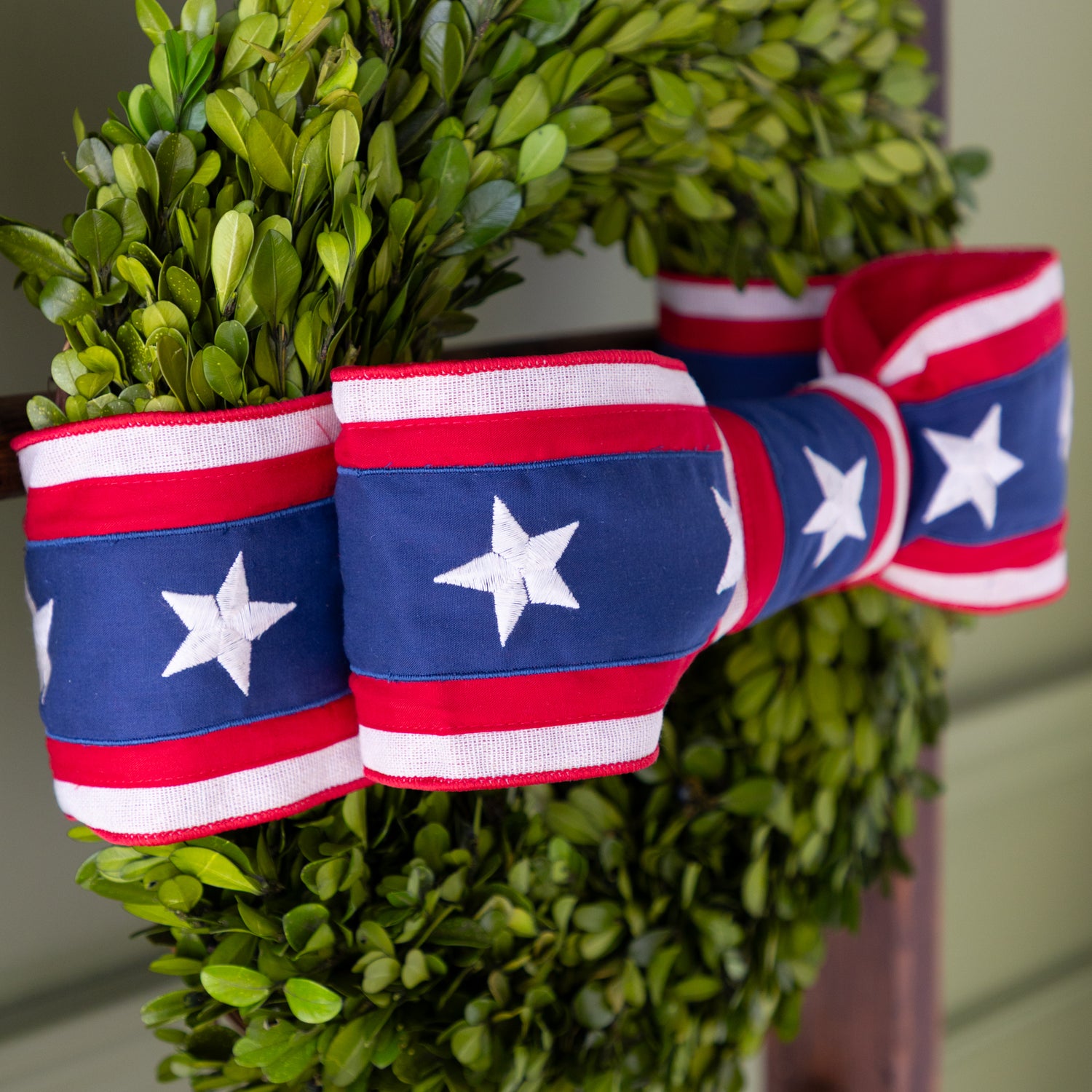 Green boxwood wreath with American flag ribbon tied around it.