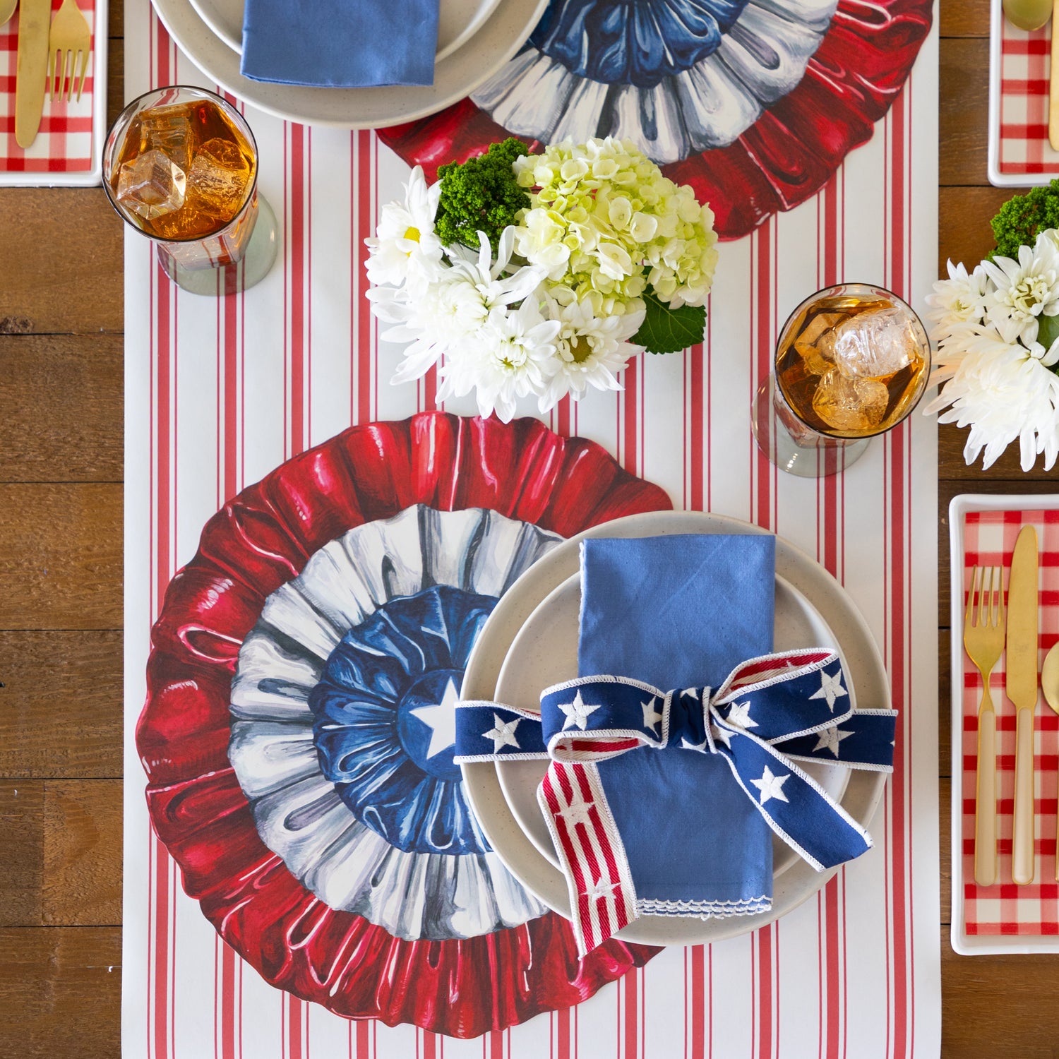 Table setting with patriotic table setting including a set of plates and napkins tied with a ribbon on a red and white striped runner. 