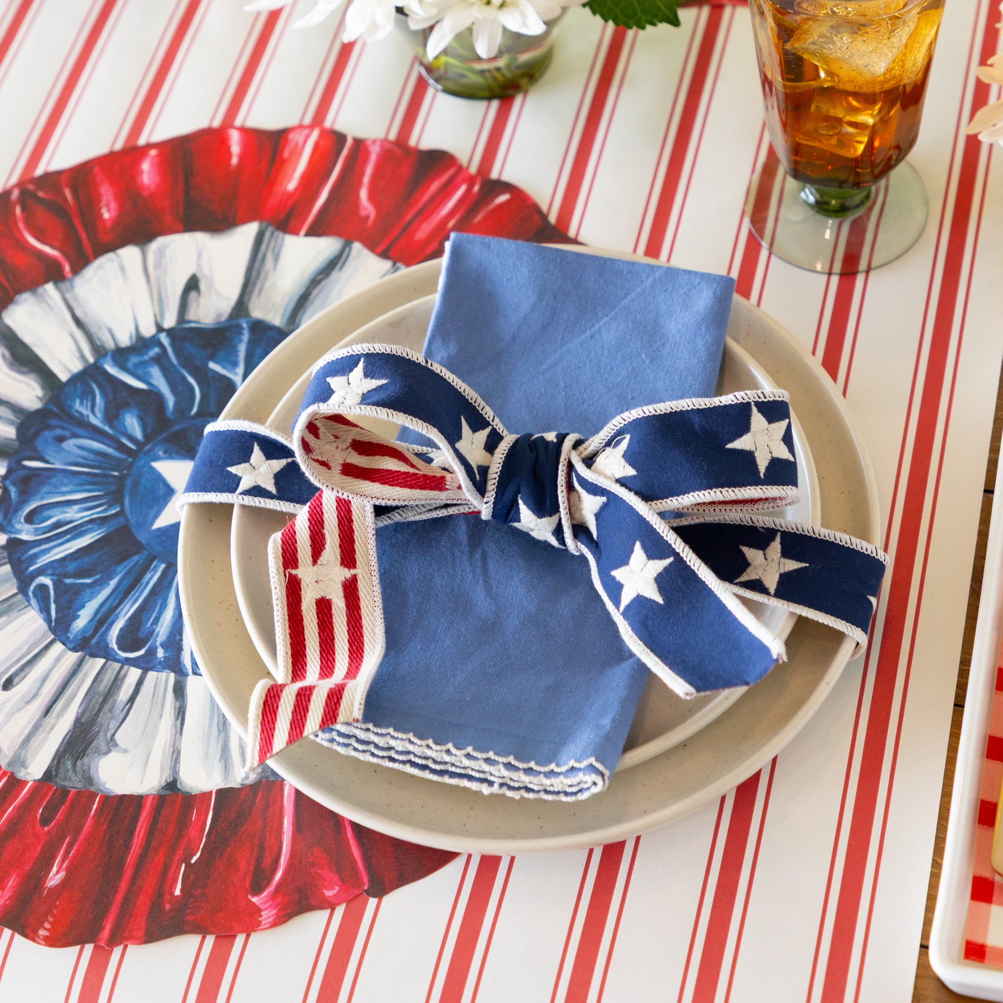 Decorative table setting with red, white, and blue ribbon tied around napkins on a striped tablecloth.