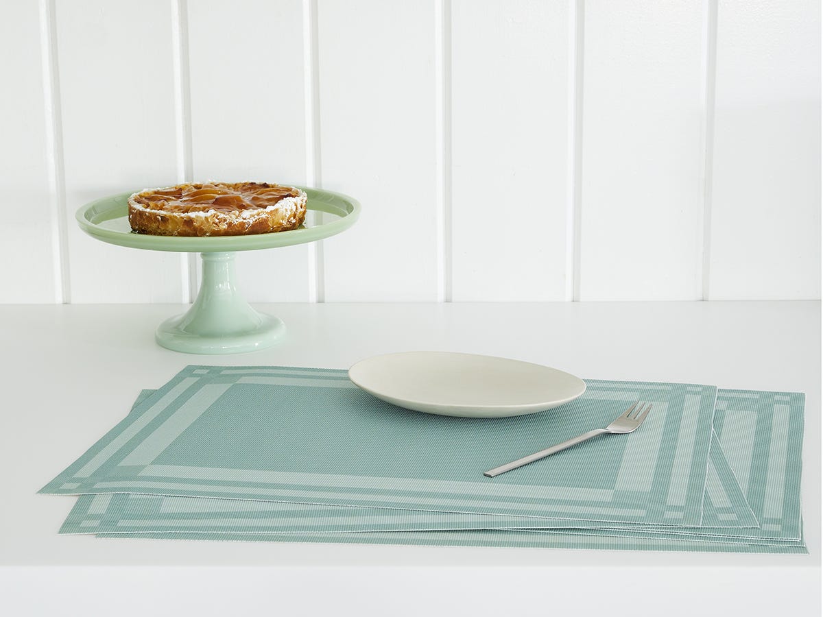 Scattered stack of the Abalone Handkerchief Compact Rectangle Placemat with a plate and fork on top and in the background a cake stand with a pie on it. 