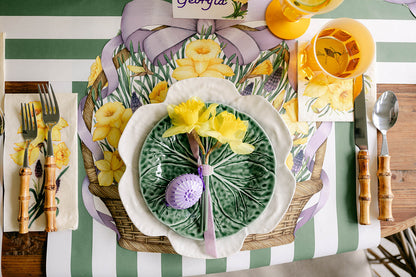 An illustrated wicker basket with a big purple ribbon bow on the handle, full of vibrant yellow daffodils and purple blooms with green foliage, on a white background.