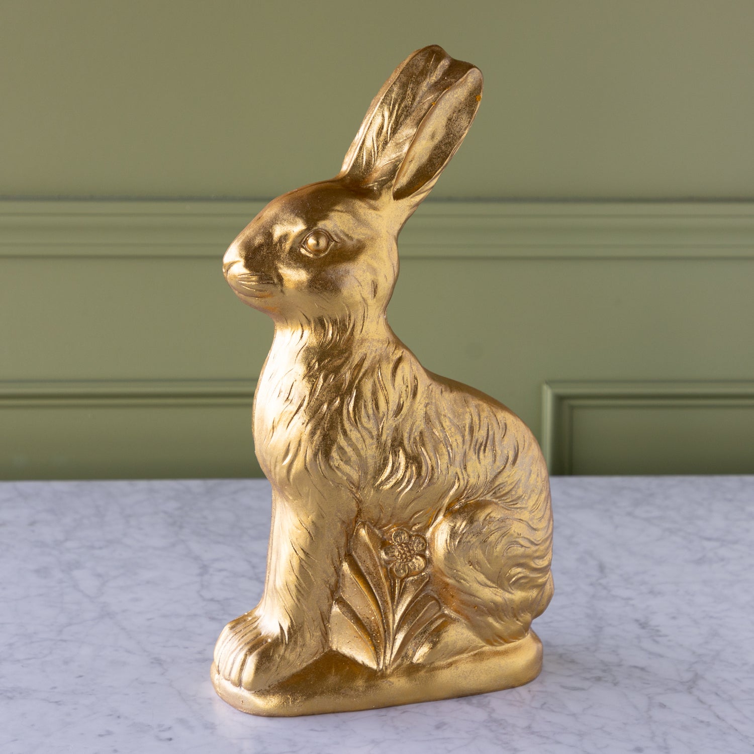 Gold rabbit figurine on a marble surface with a green wall background.