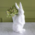 White rabbit-shaped vase with green hydrangeas against a green wall.