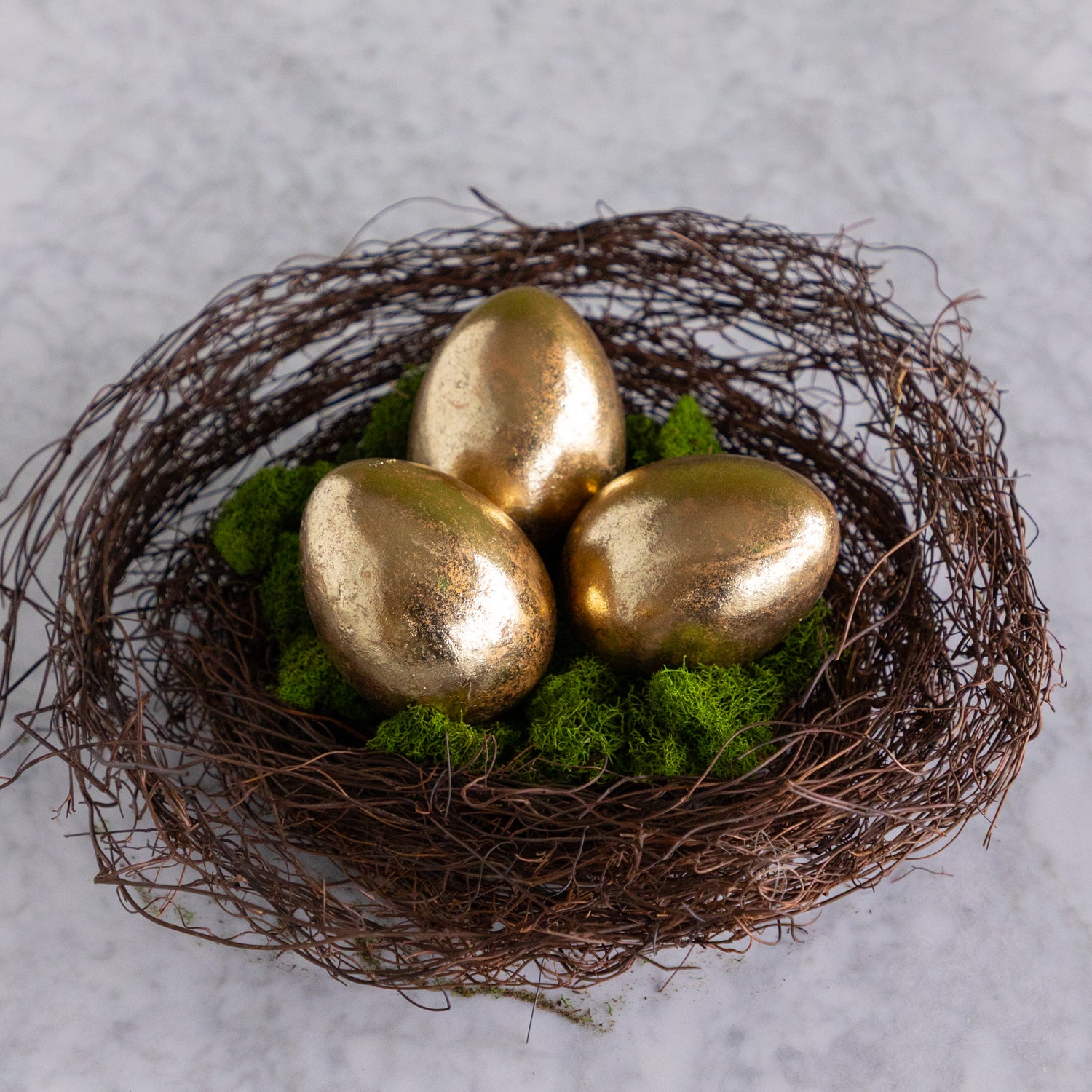Three gold eggs in a nest with green moss on a light gray background.