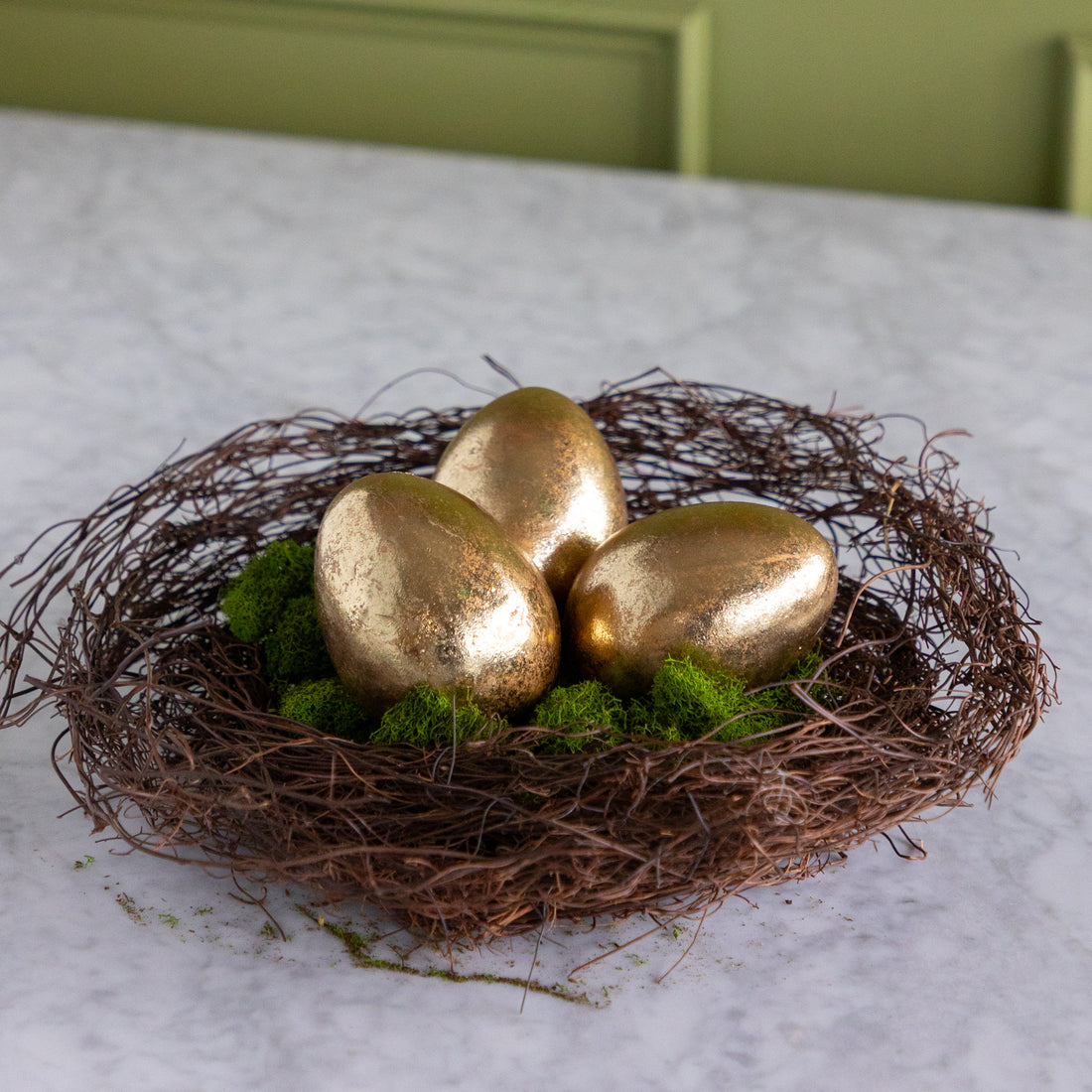 Three gold eggs in a nest on a marble surface with a green background.