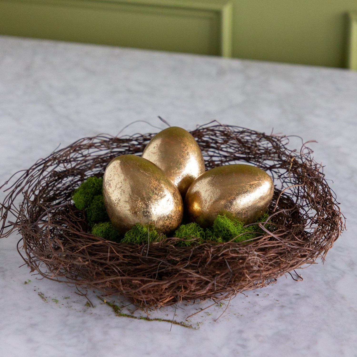 Three gold eggs in a nest on a marble surface with a green background.