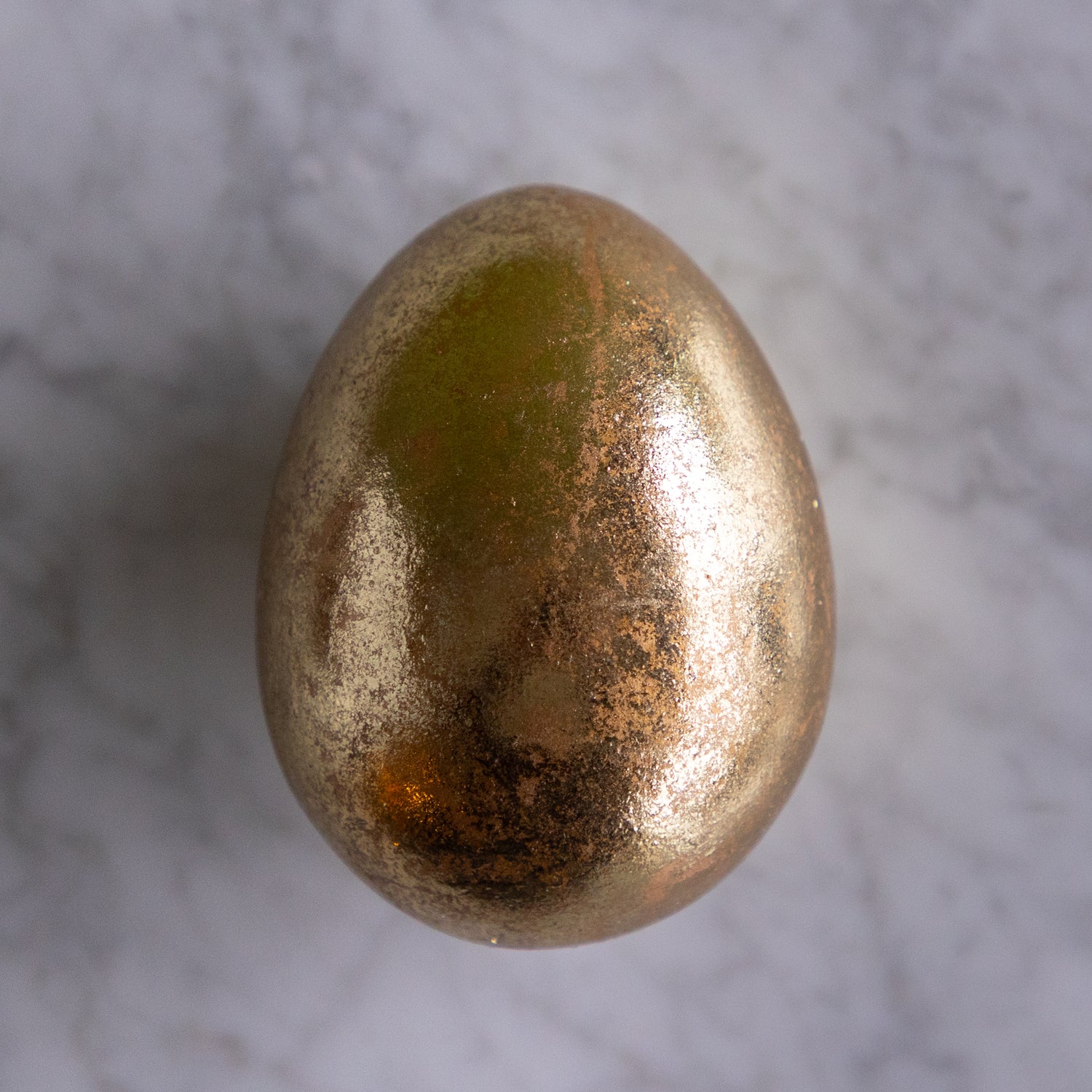 Bronze-colored egg on a gray marble surface.