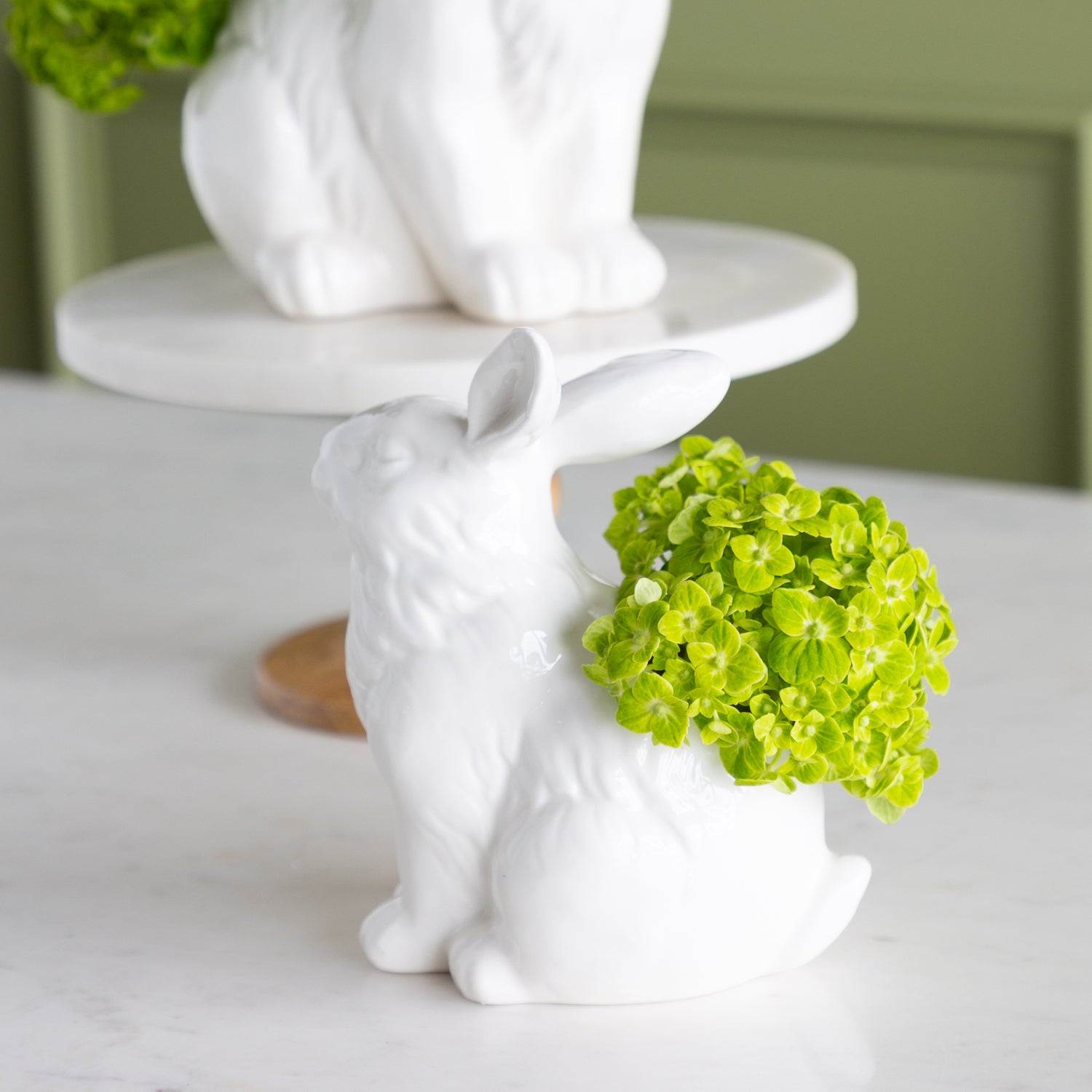 White ceramic rabbit figurine with green flowers on a white surface.