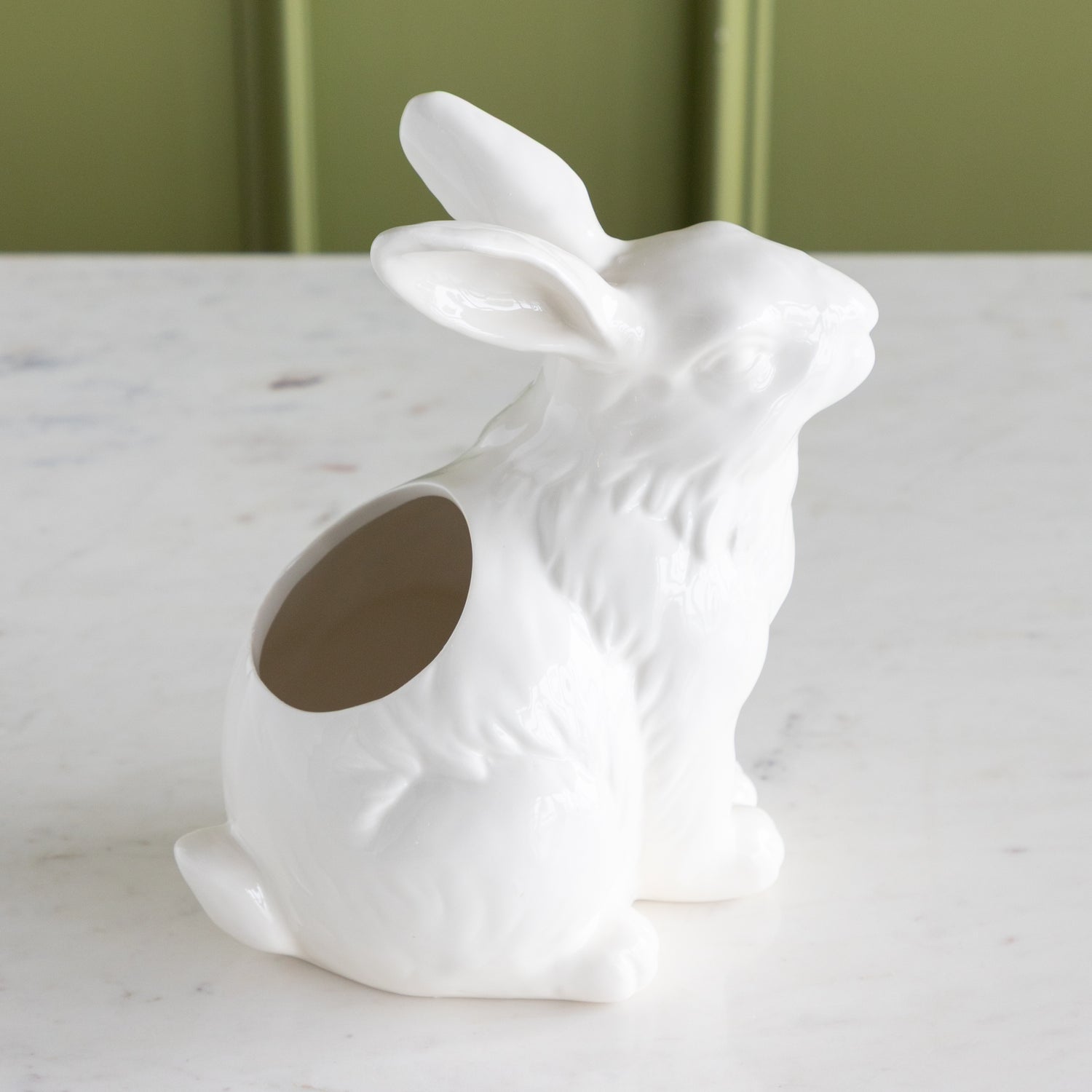 White ceramic rabbit-shaped vase on a marble surface with a green background.