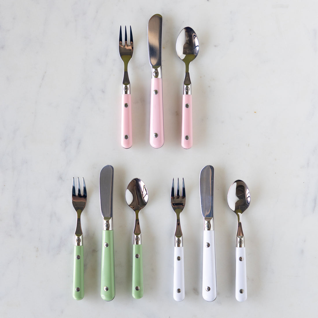 A set of flatware with pink, white, and green handles, including forks, knives, and spoons, displayed on a marble surface.