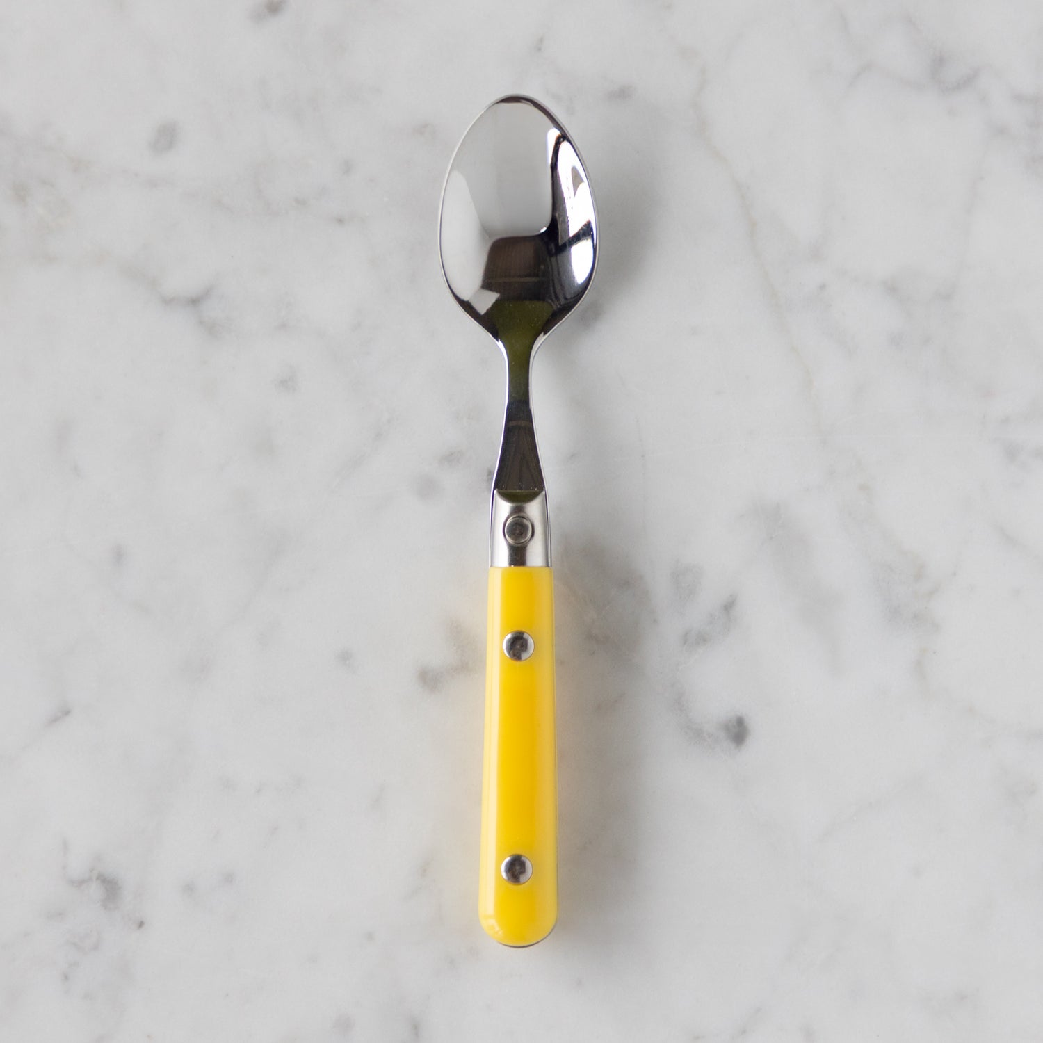 Spoon with a yellow handle on a marble background.