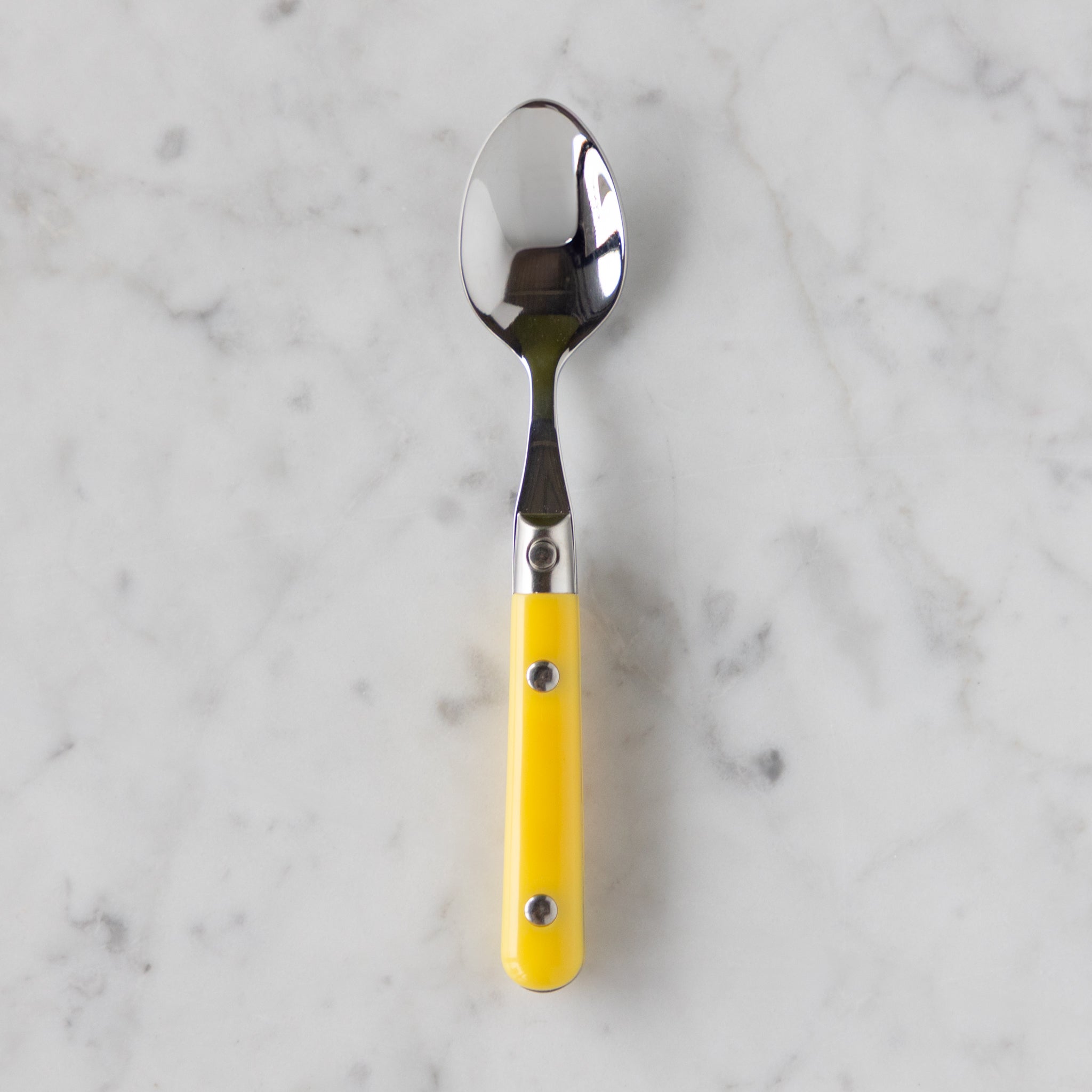 Spoon with a yellow handle on a marble background.
