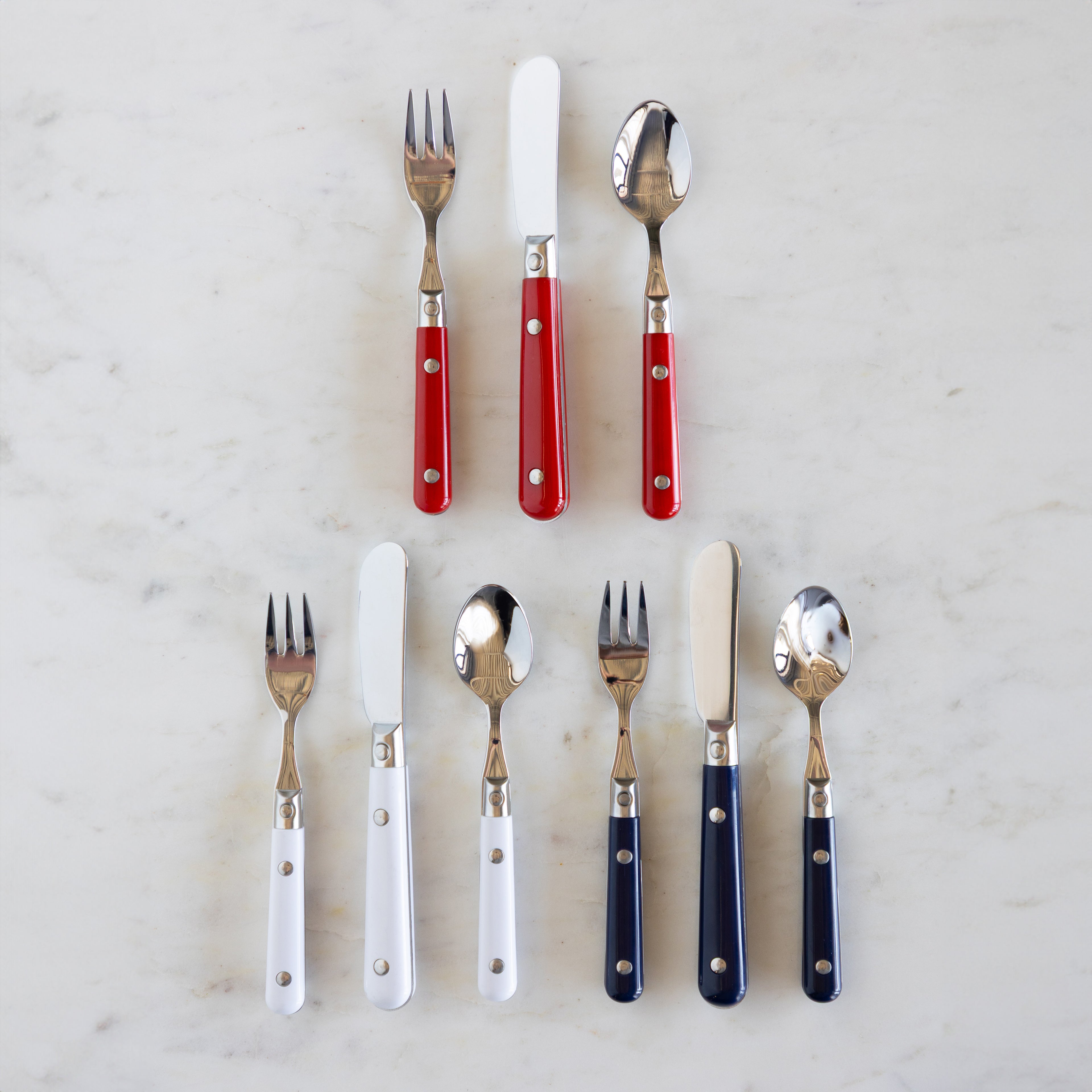 A set of flatware with red, white, and blue handles, including forks, knives, and spoons, displayed on a marble surface.