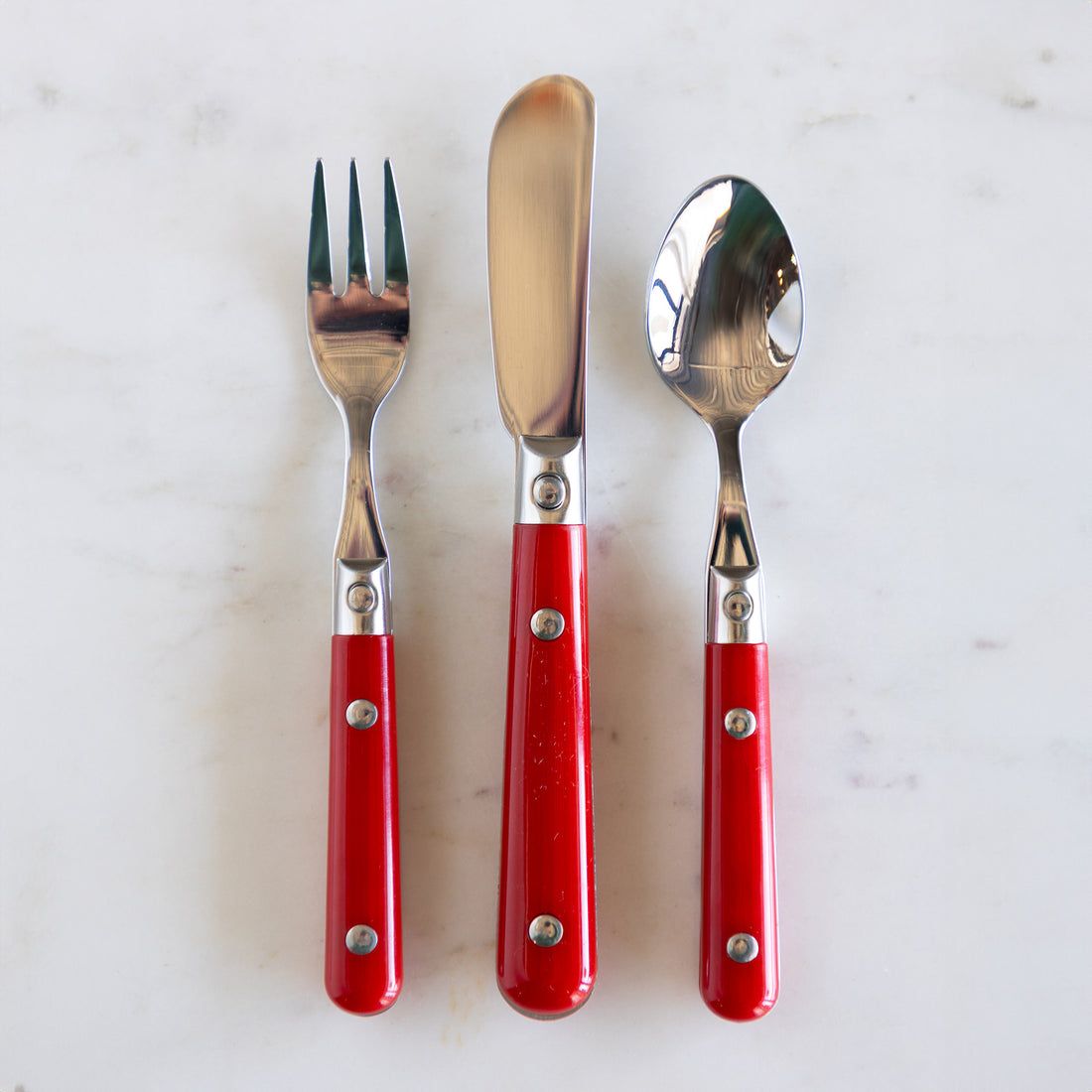 A spoon, knife and fork with red handles. 