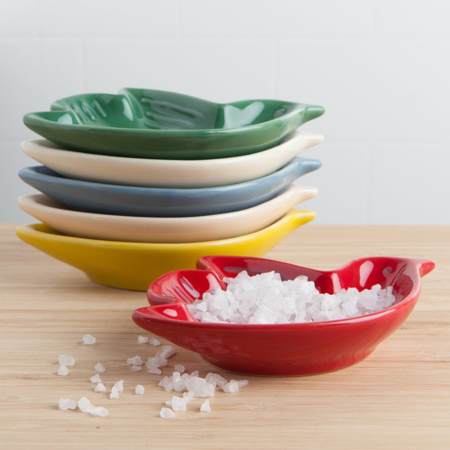 Set of colorful ceramic bowls on a wooden surface with a red bowl containing salt.