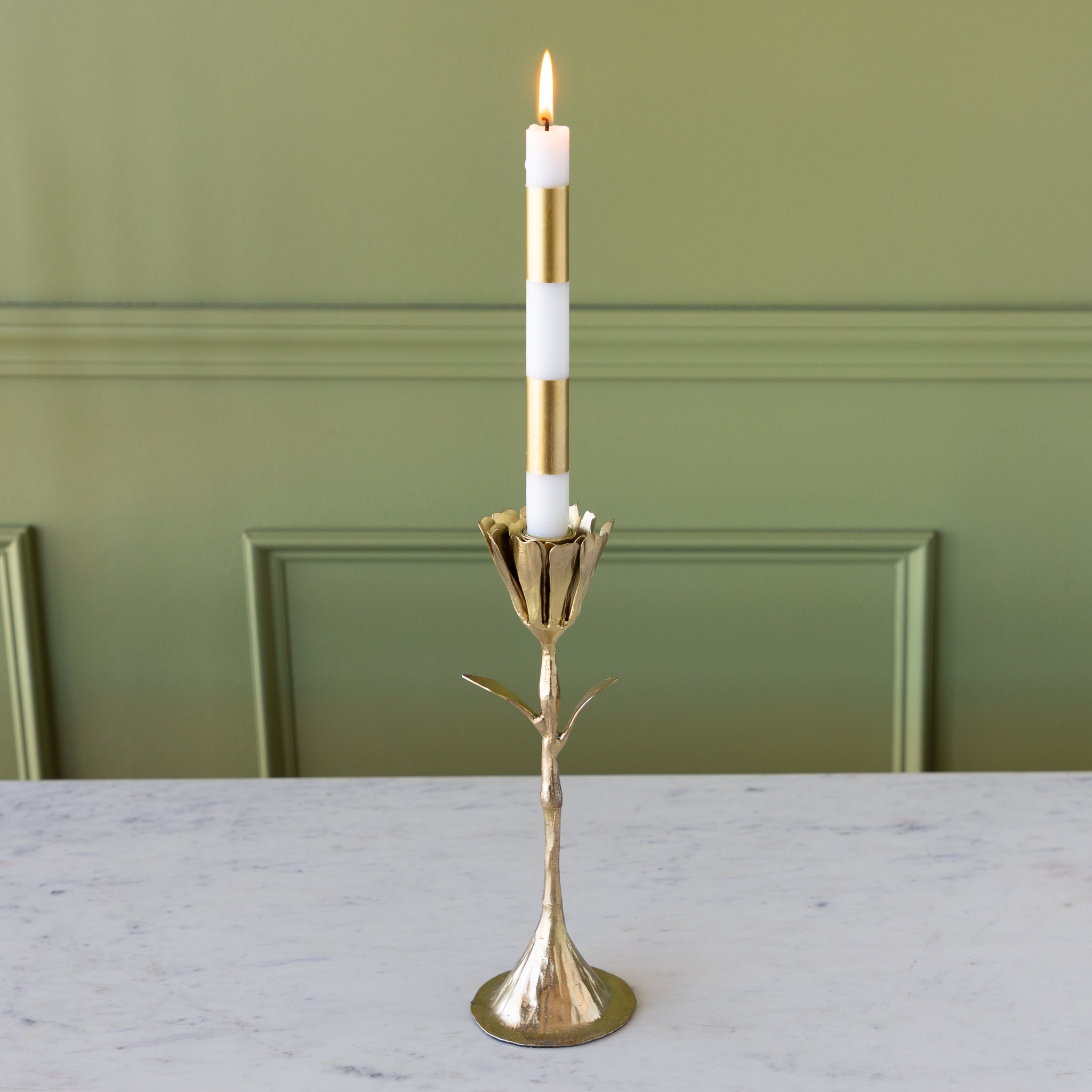 Gold candle holder with a white candle on a marble surface against a green wall.