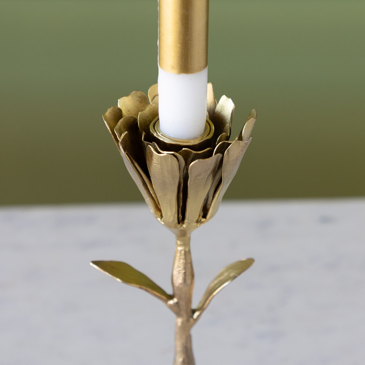 Gold candle holder with a white candle against a green background.