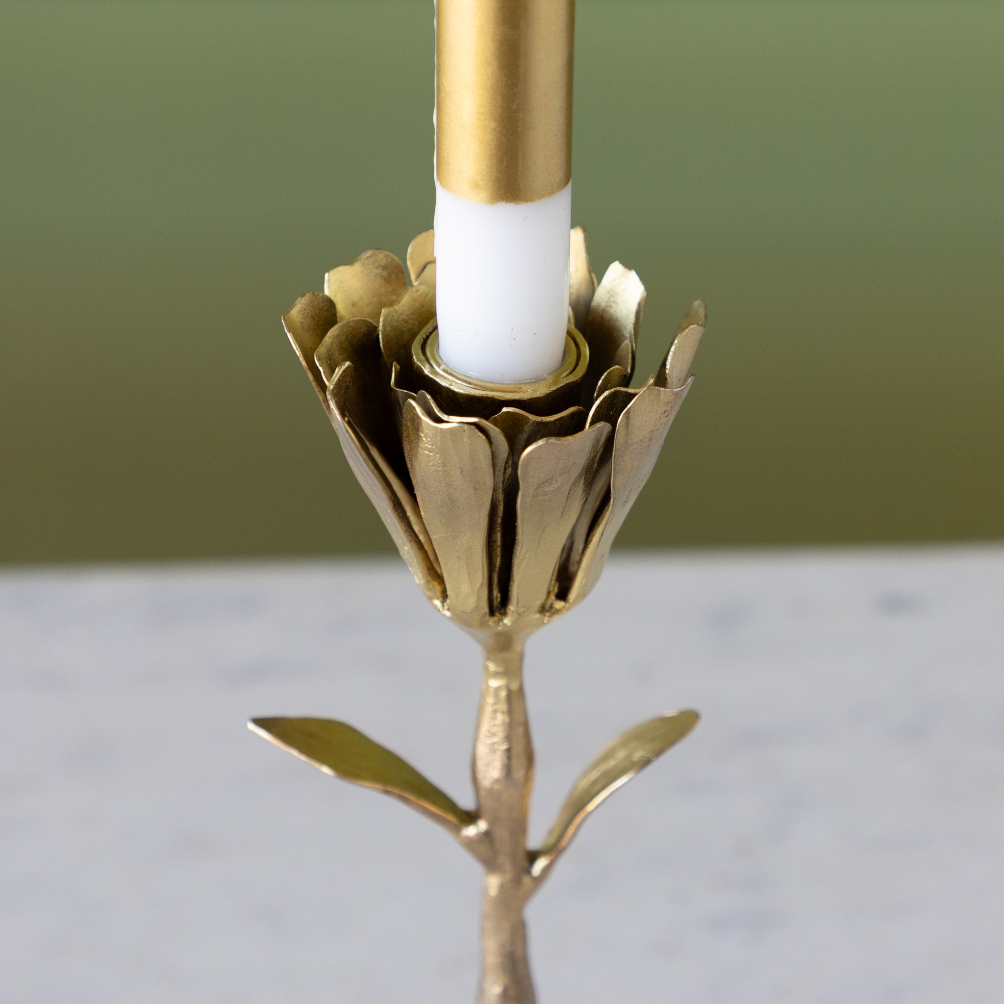 Gold candle holder with a white candle against a green background.