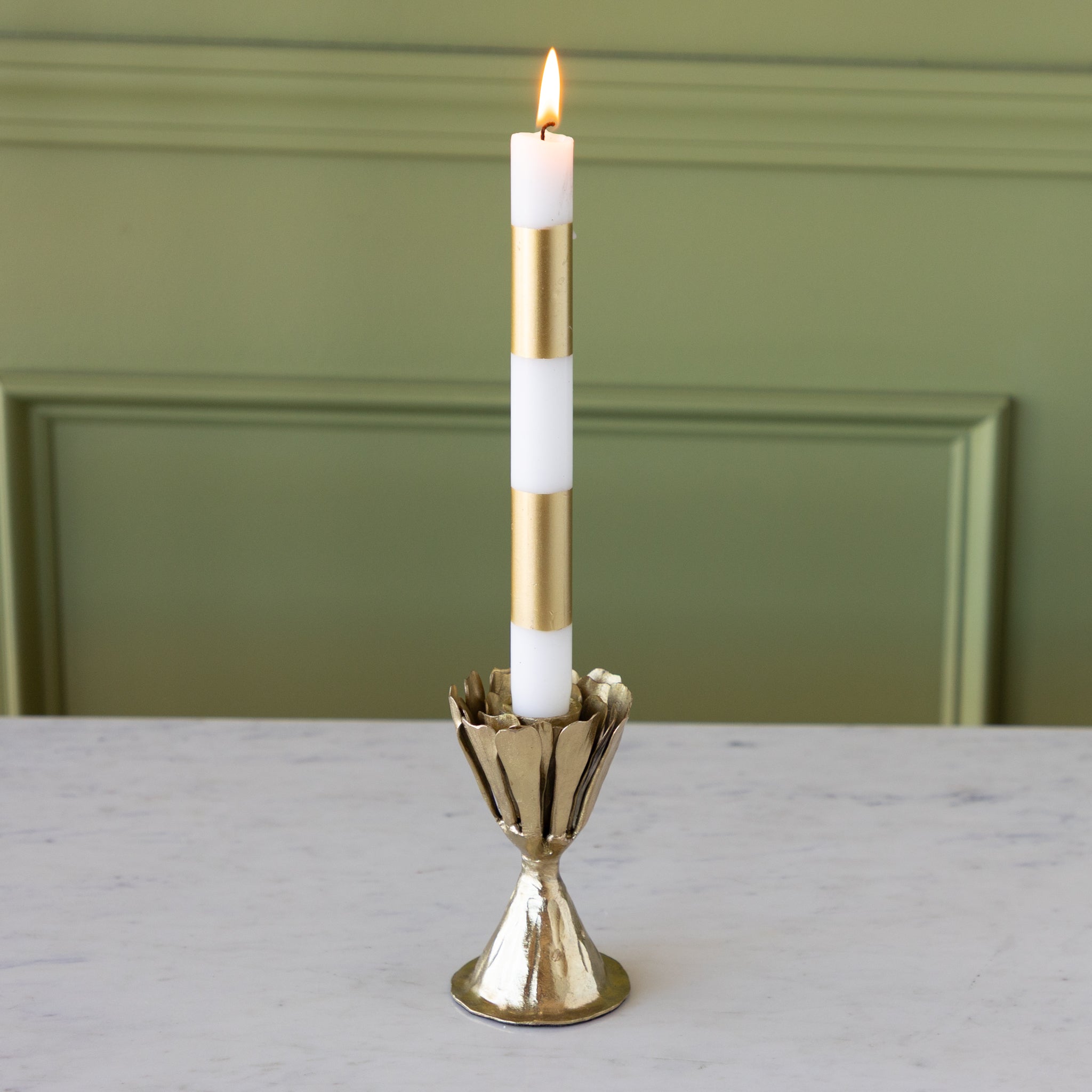 Gold candle holder with a white candle on a marble surface against a green wall.