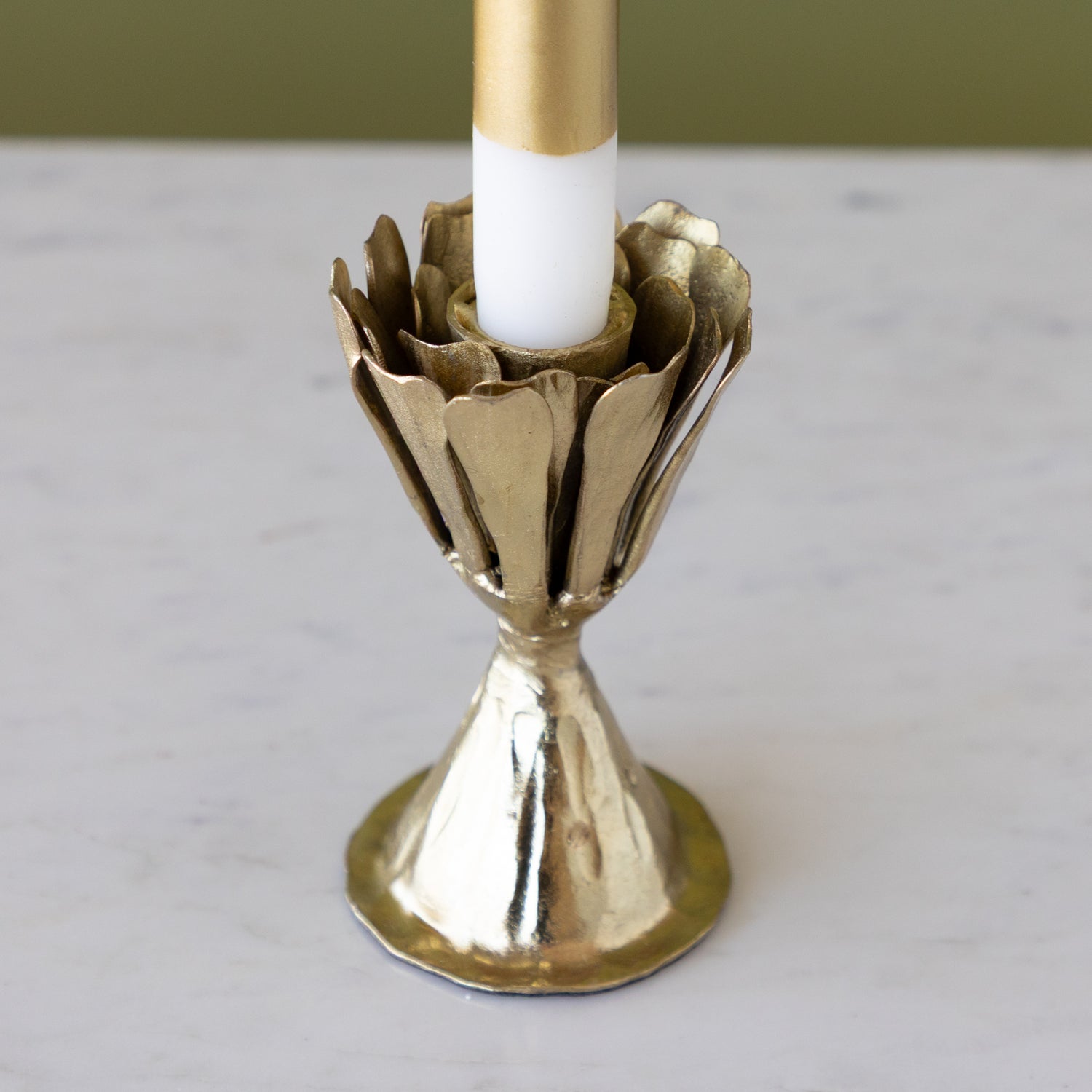 Gold candle holder with a white candle on a light gray surface.
