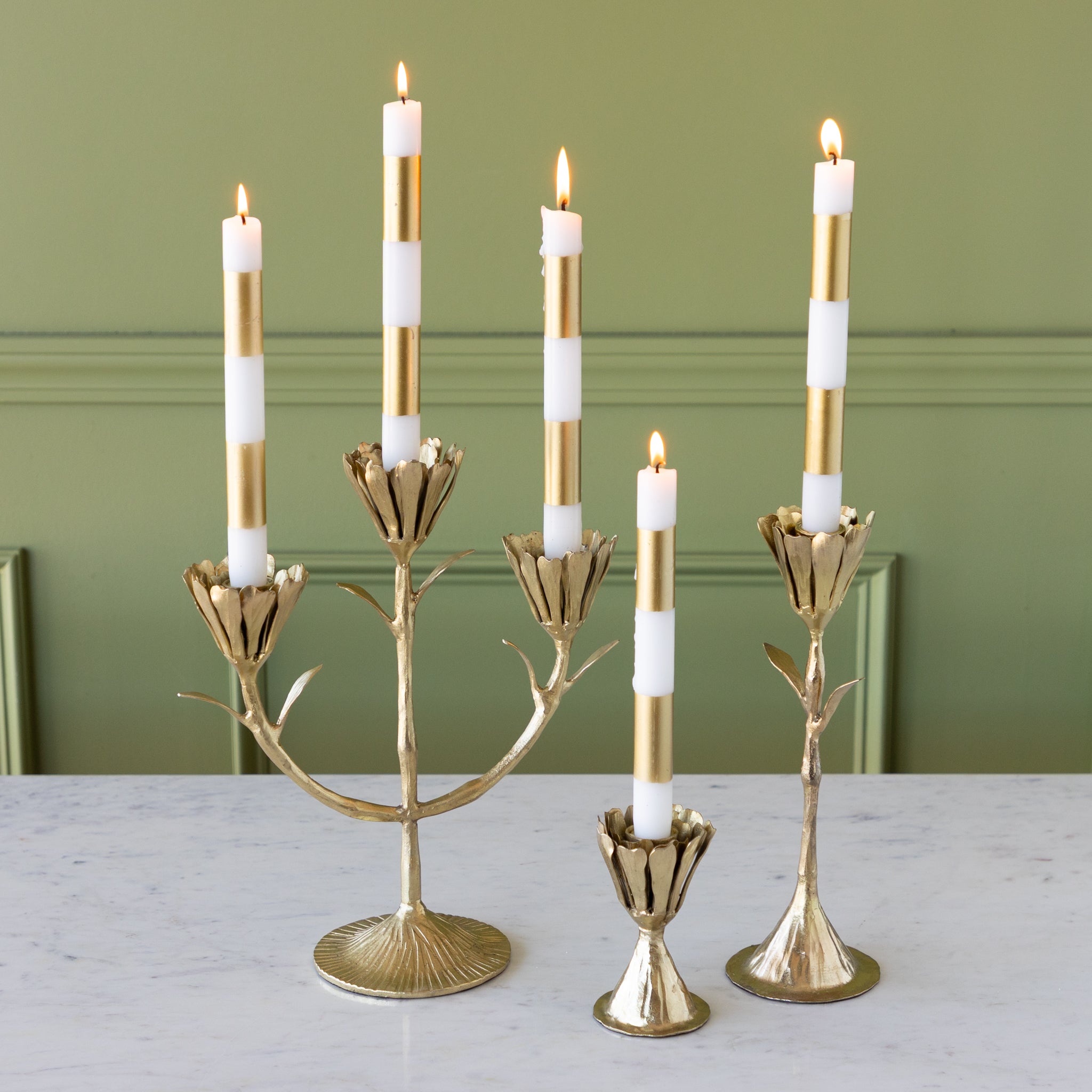 Set of gold candle holders with white candles on a table against a green wall.