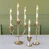 Set of gold candle holders with white candles on a table against a green wall.