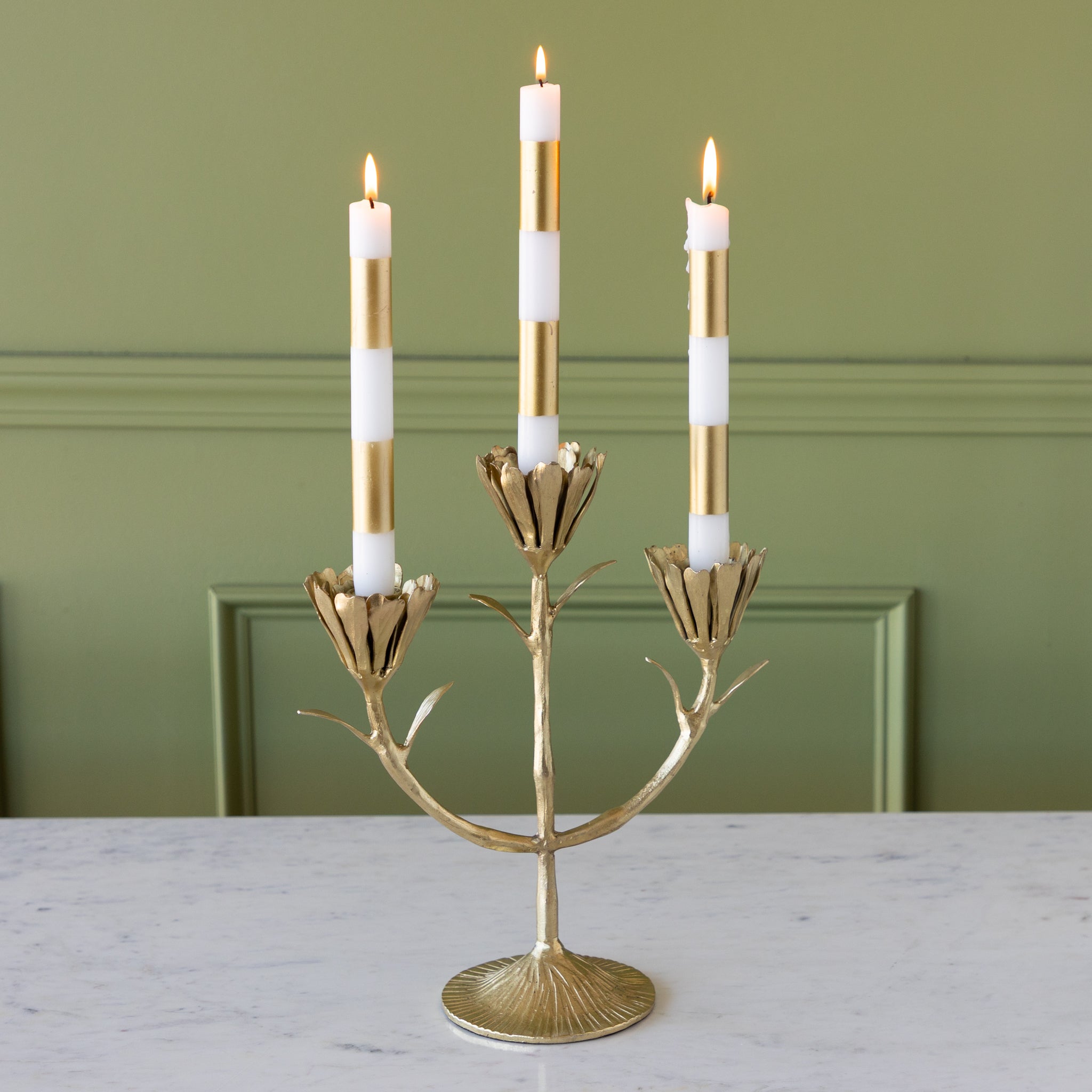 Gold candelabra with three lit candles against a green wall.