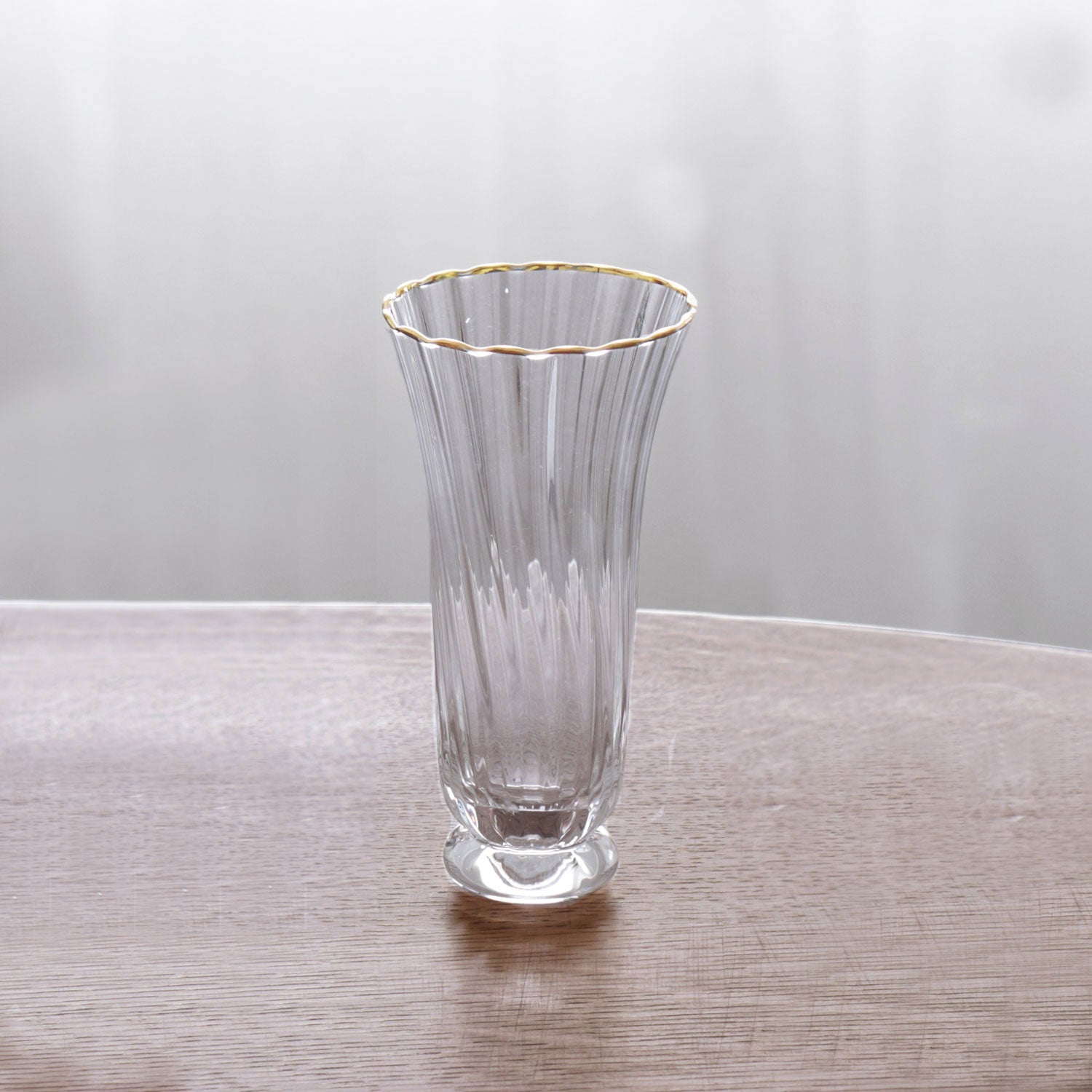 Clear glass stemless champagne flute with gold rim on a wooden surface