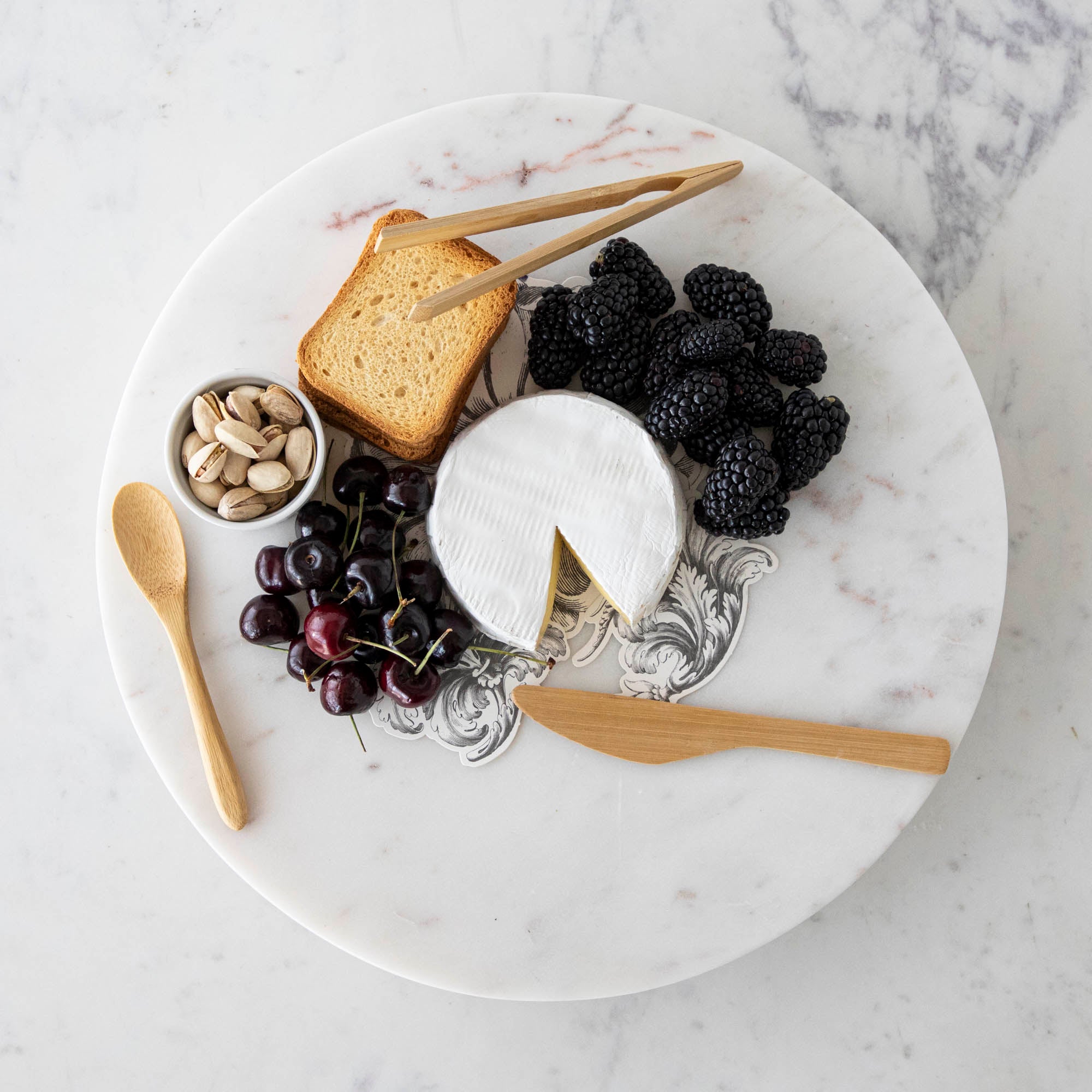 A plate with cheese, fruit, and nuts on it, served with BIA Mini Bamboo Utensils.