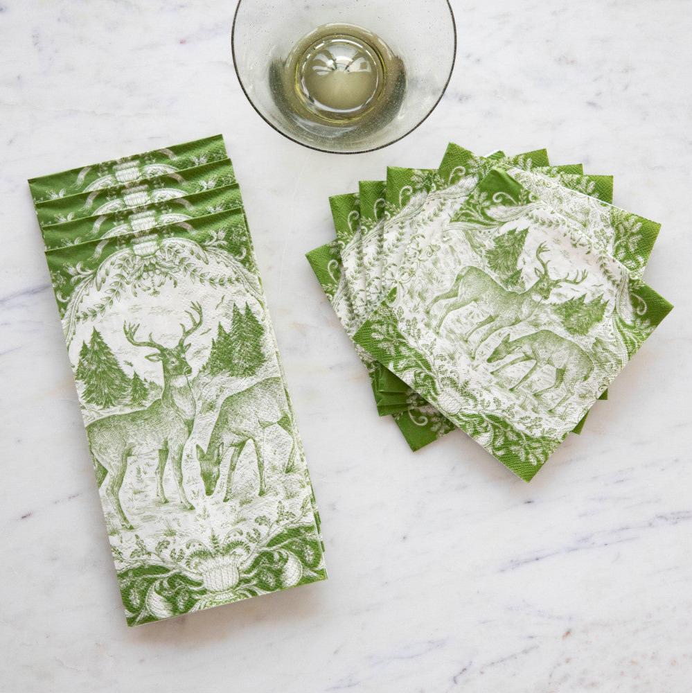 A stack of Fable Toile Guest Napkins and a fanned-out stack of Fable Toile Cocktail Napkins on a table next to a wine glass, from above.