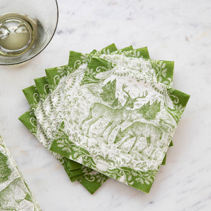 A fanned-out stack of Fable Toile Cocktail Napkins on a table next to a wine glass.