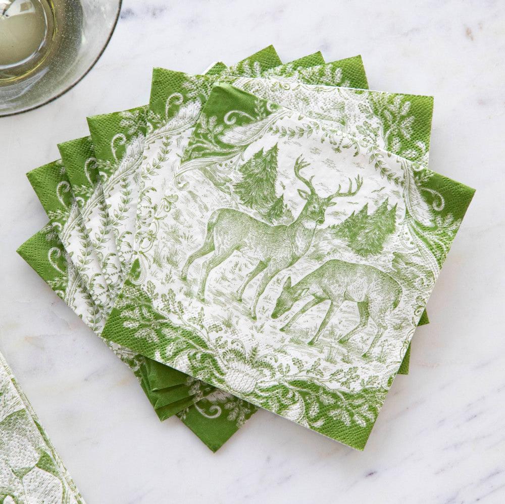 A fanned-out stack of Fable Toile Cocktail Napkins on a table next to a wine glass.