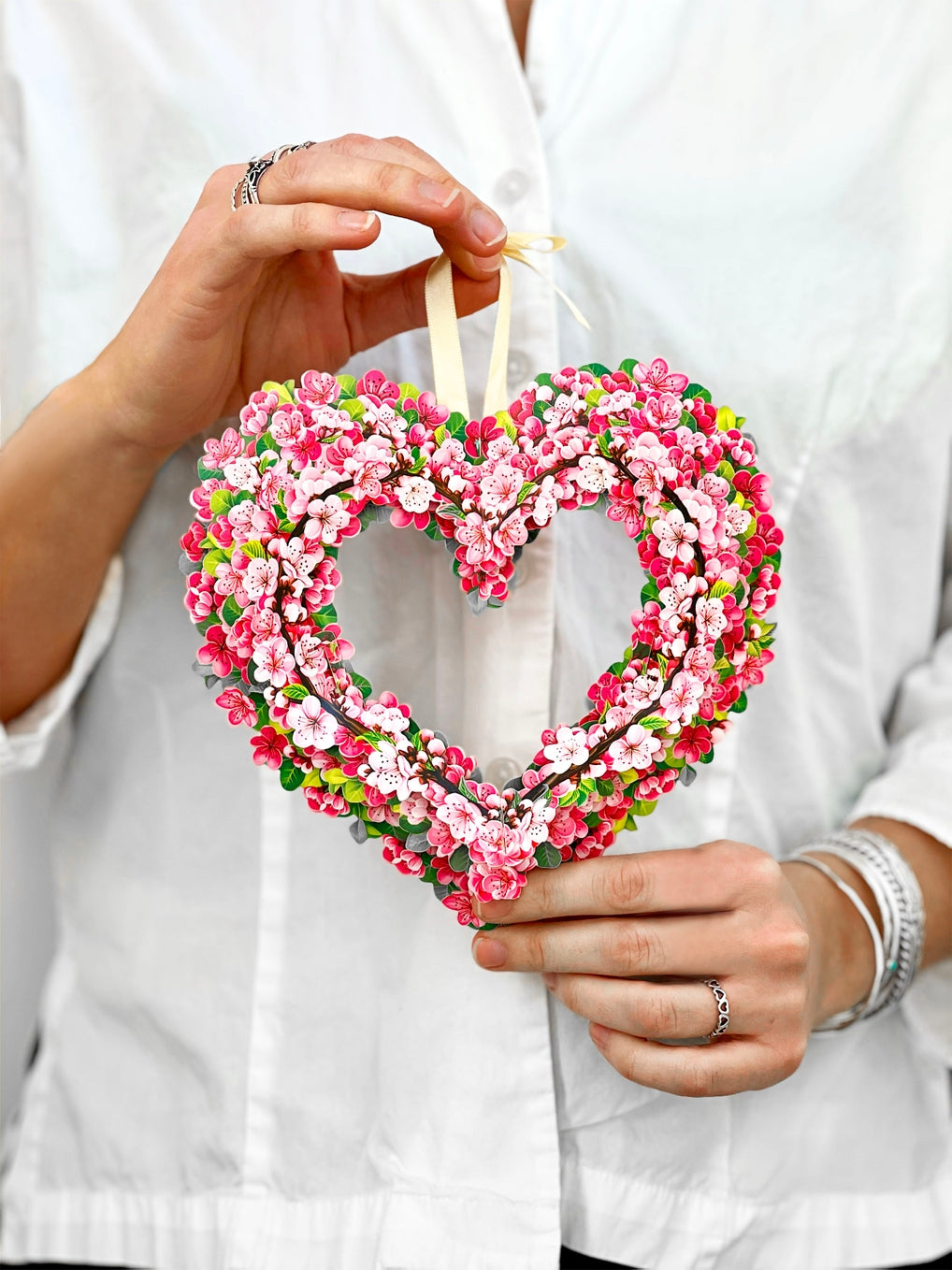 Heart-shaped paper wreath with cherry blossoms held by a person against a white background.