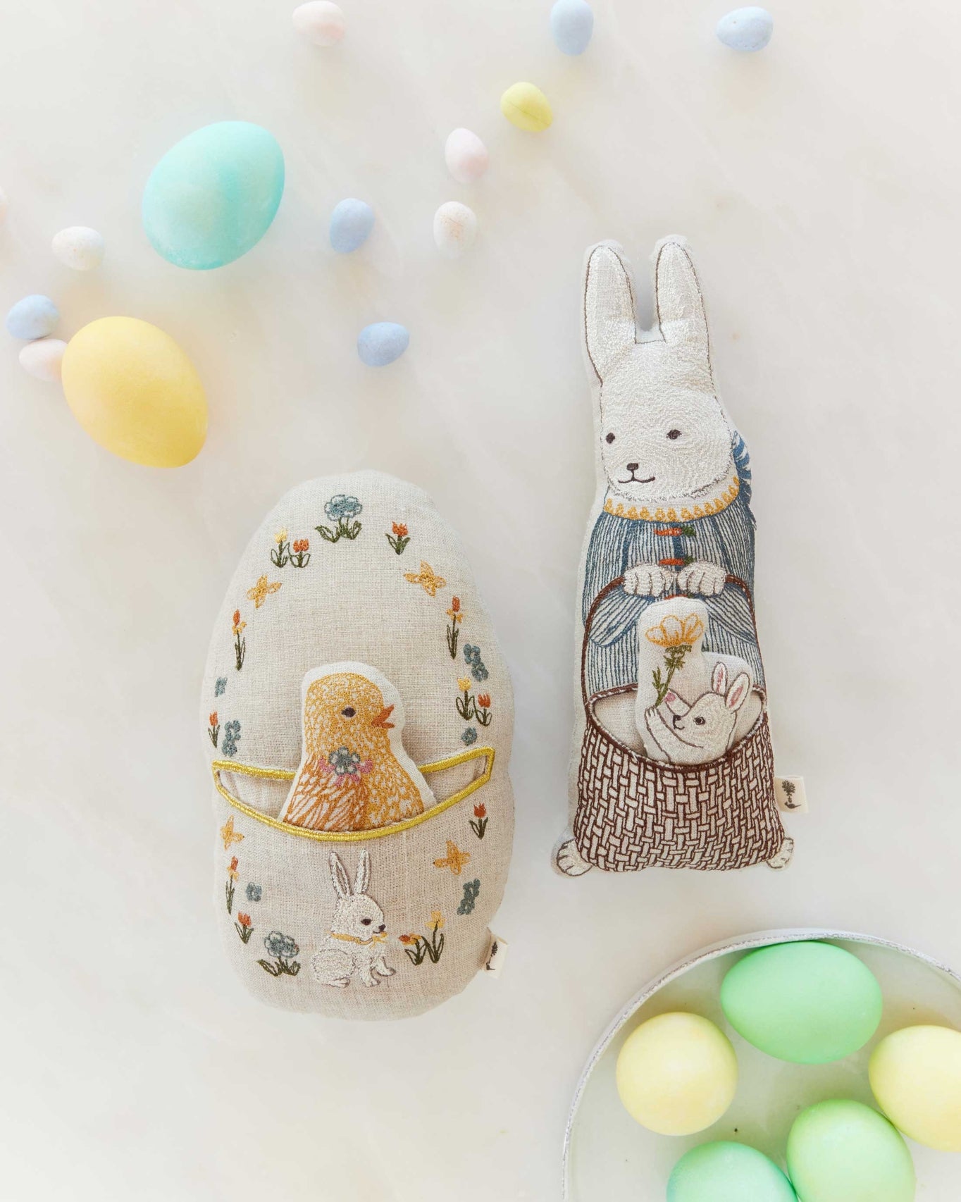Decorative Easter eggs with embroidered designs and a rabbit figure on a light background.