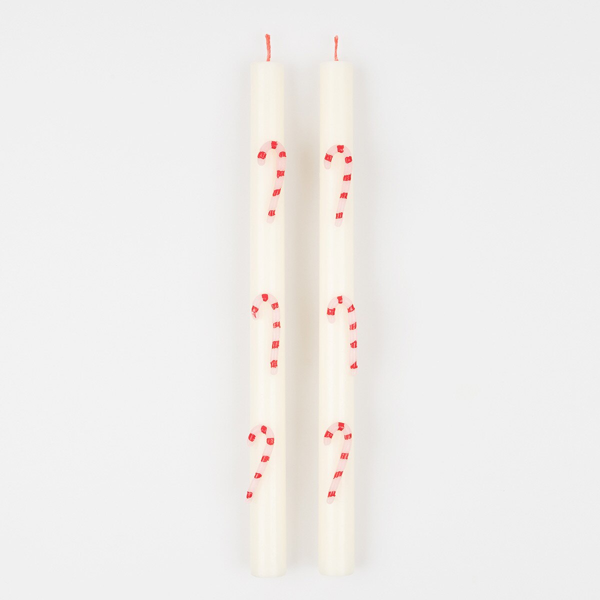 Two white taper candles with red candy cane designs printed on them, shown against a plain white background.