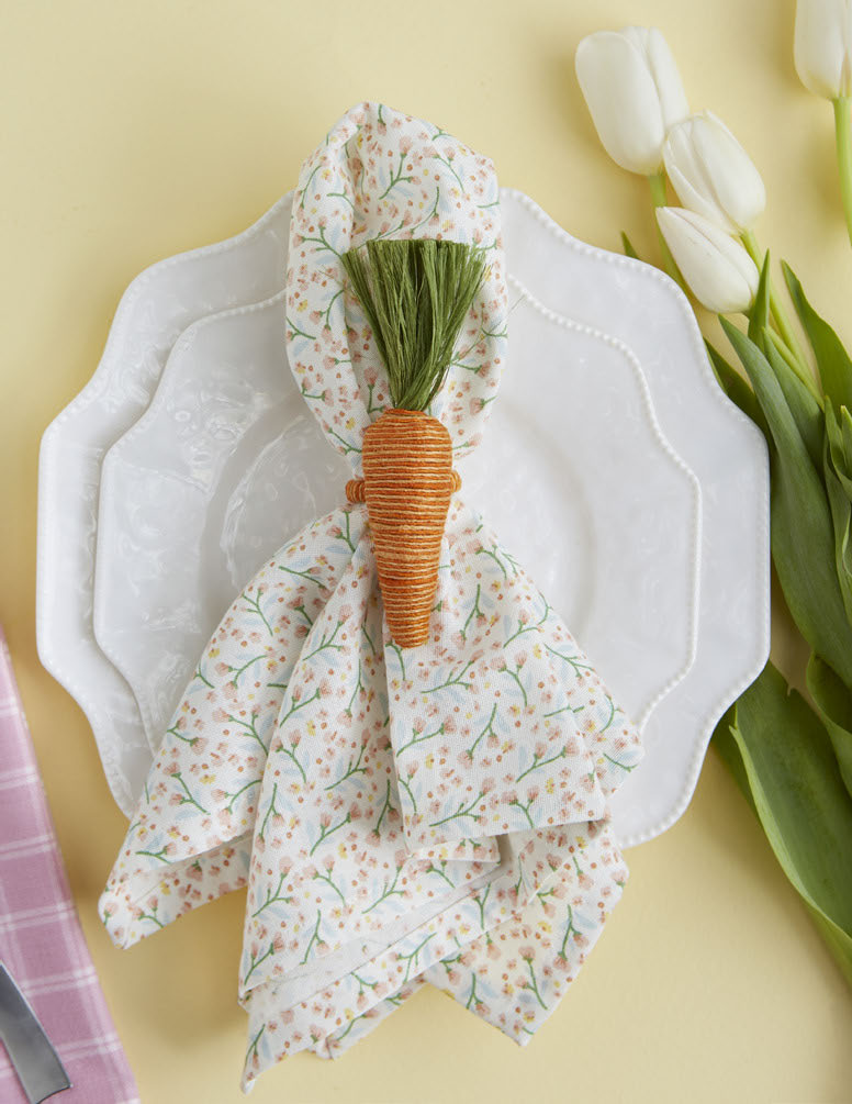 Floral napkin with carrot holder on a white plate with tulips in the background.