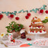 Decorative table setting with a cake, plants, and colorful plates on a beige background.