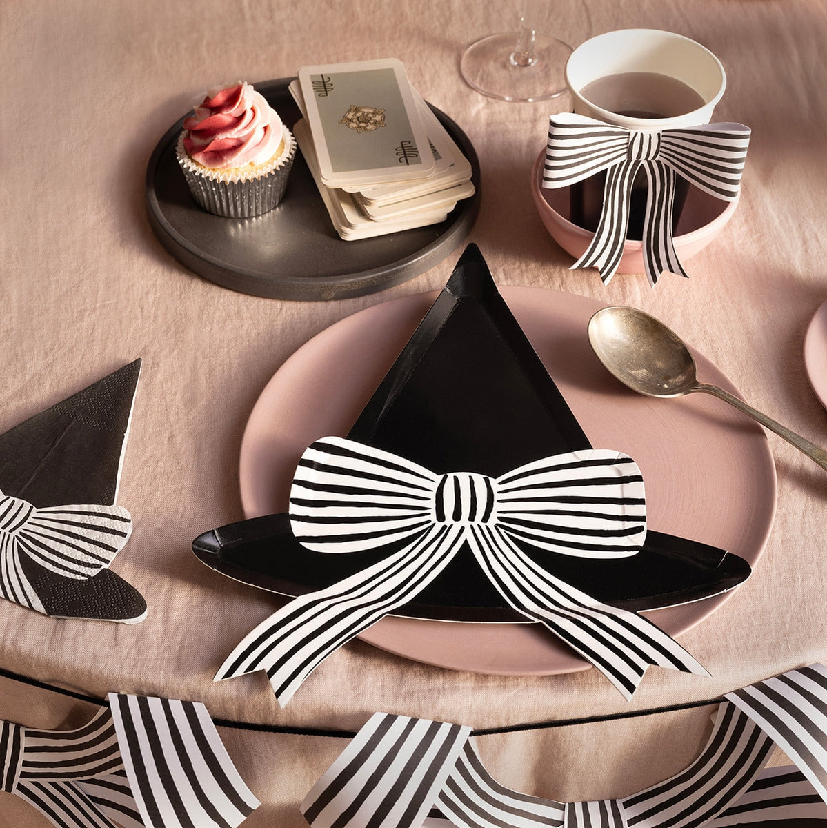 Table setting with Witch Hat plates and cups with black and white striped bow decorations on a pink tablecloth.