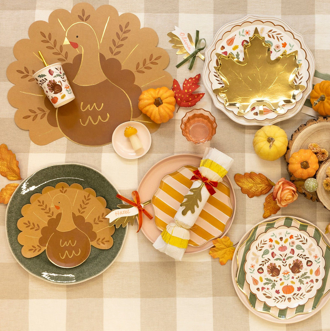 Thanksgiving-themed table setting with decorative plates, napkins, and pumpkins on a checkered tablecloth.