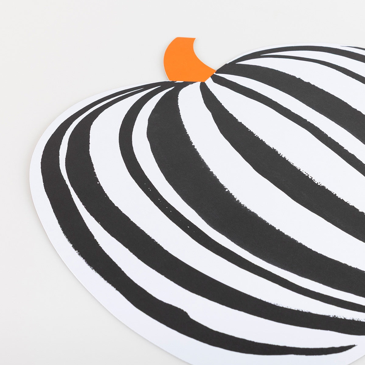 Black and white striped pattern paper placemat in the shape of a pumpkin with an orange top on a light gray background. 