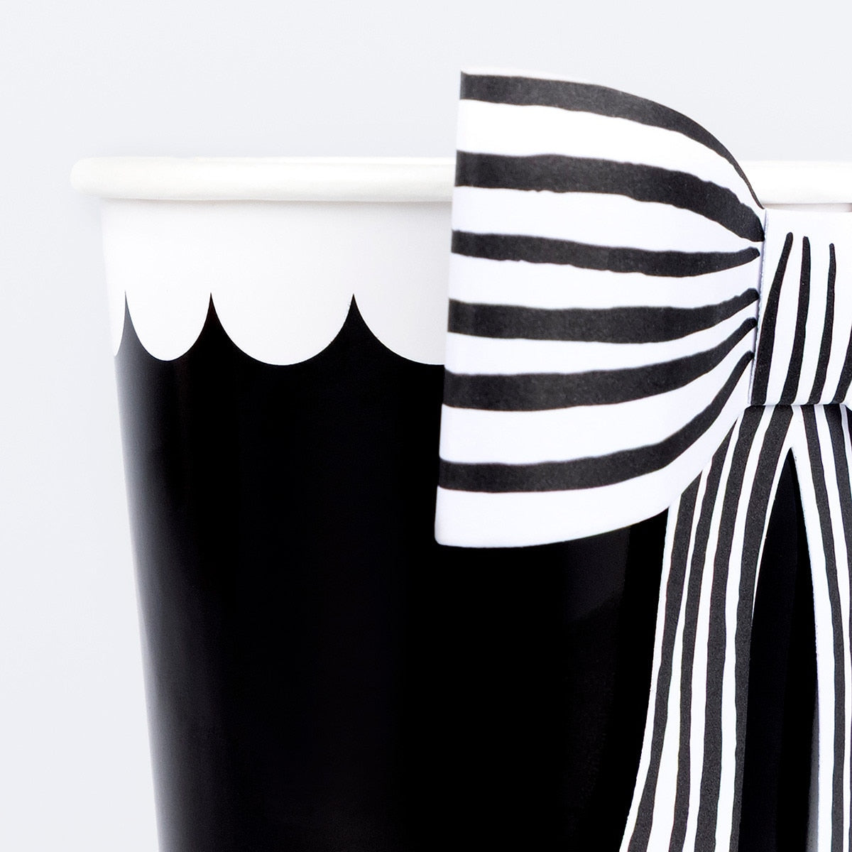 Black paper cup with a black and white striped paper bow attached to it. 