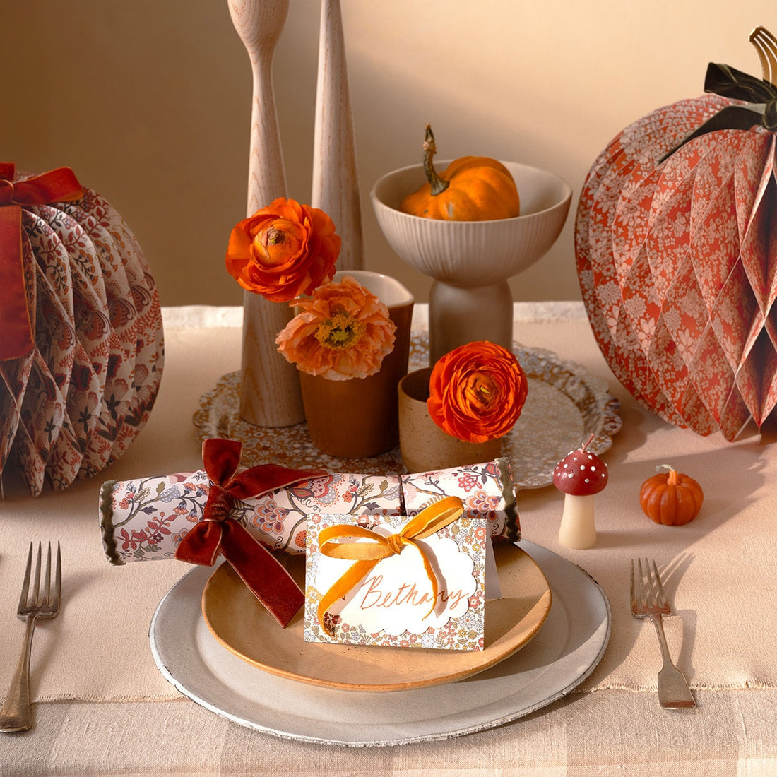 Decorative table setting with pumpkins, flowers, and gift boxes on a checkered tablecloth.