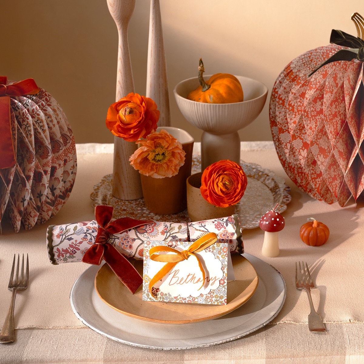 Decorative table setting with pumpkins, flowers, and gift boxes on a checkered tablecloth.