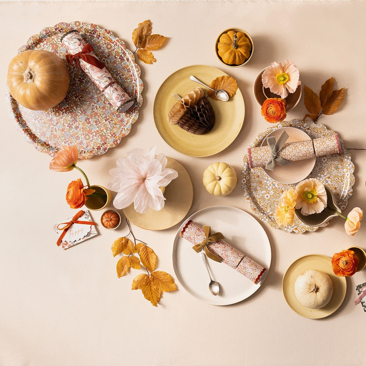 Decorative table setting with plates, flowers, and small pumpkins on a beige background