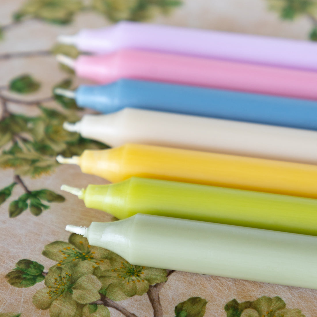 Set of colorful candles on a floral-patterned surface.