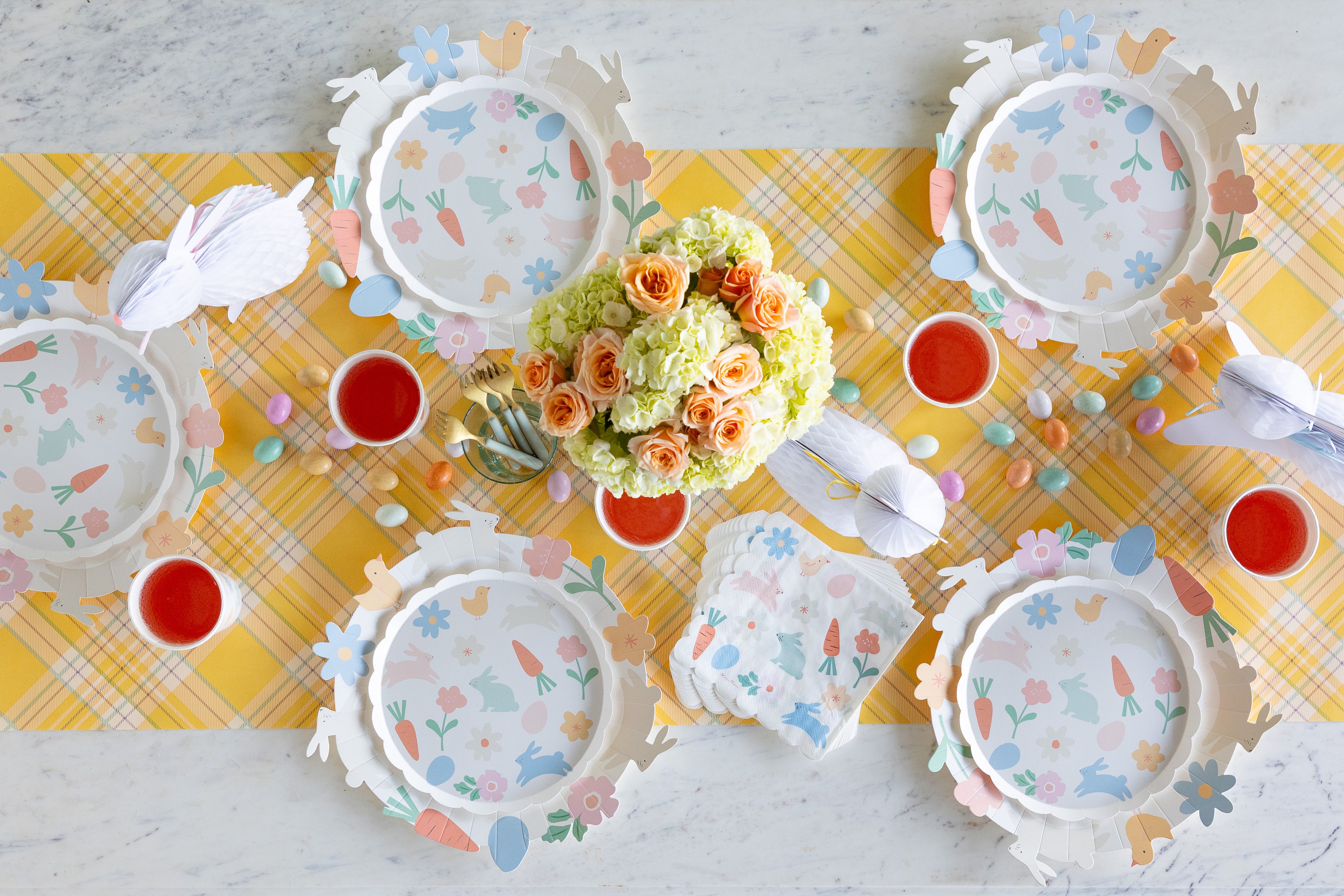 Table setting with floral centerpieces, plates, and cups on a yellow checkered tablecloth.