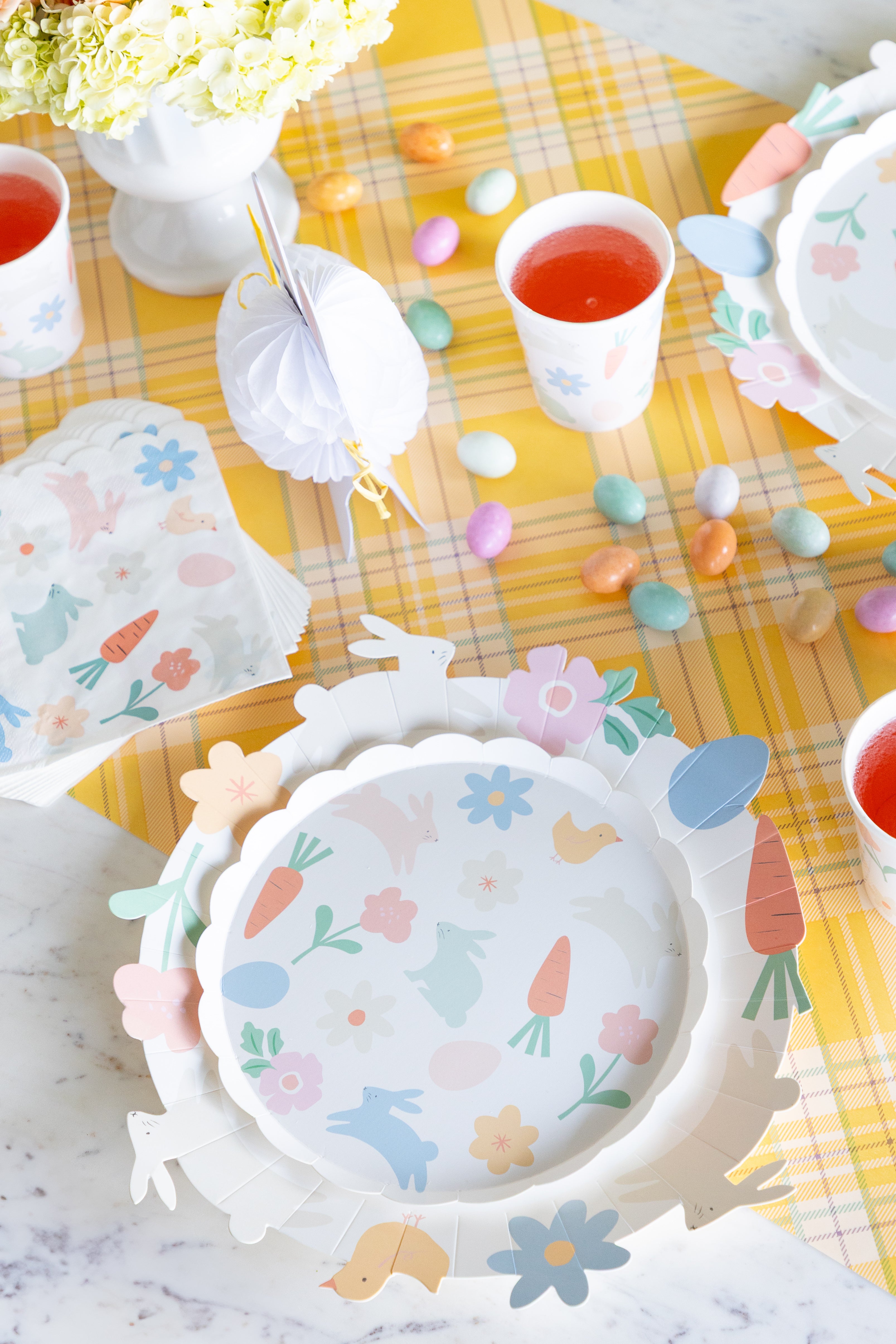 Pastel-themed table setting with plates, cups, and decorative elements on a yellow checkered table runner.