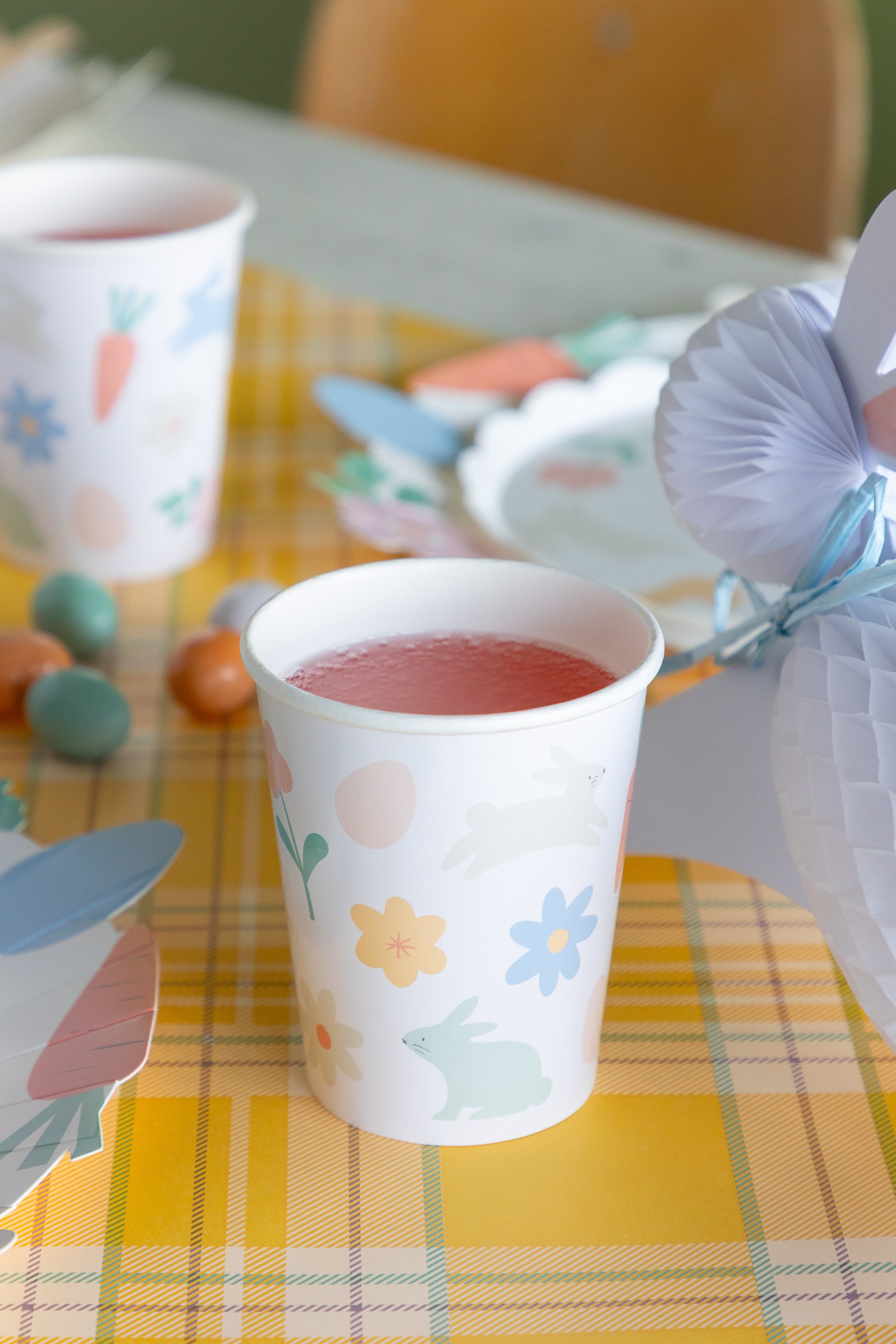 Paper cup on a yellow checkered tablecloth with Easter decorations.